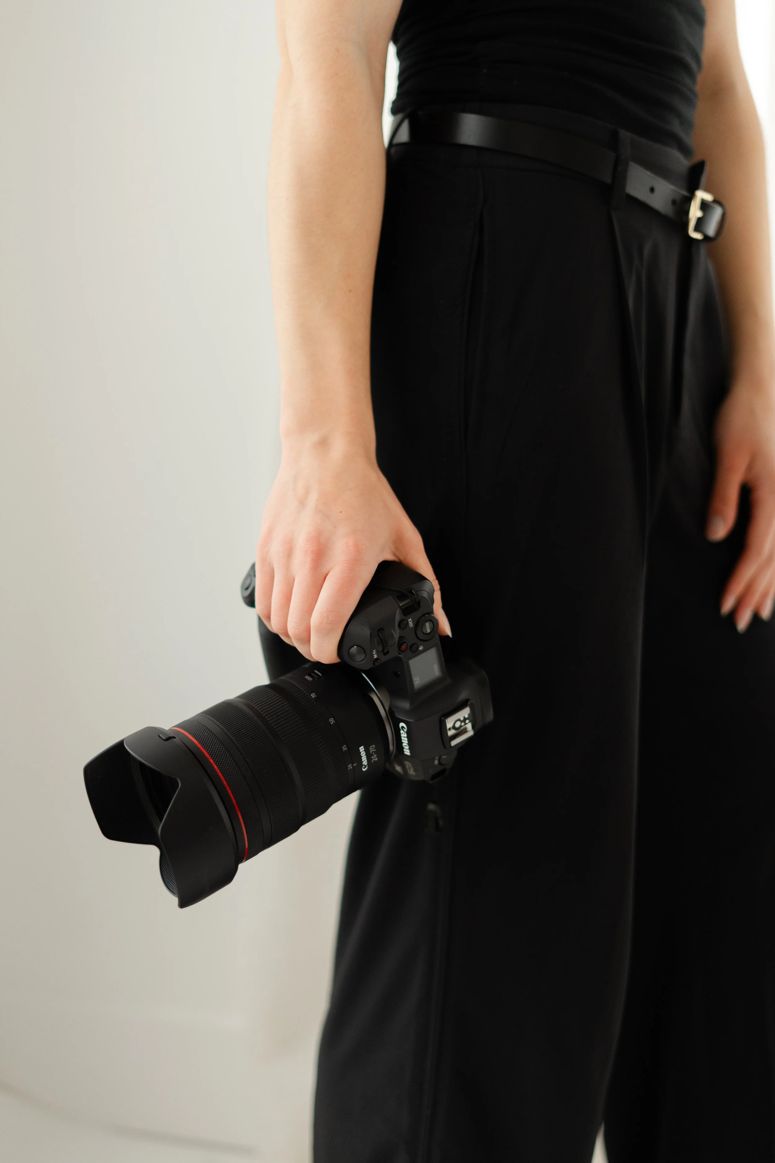 Close-up of a person wearing black clothing holding a professional camera with a large telephoto lens in their right hand.