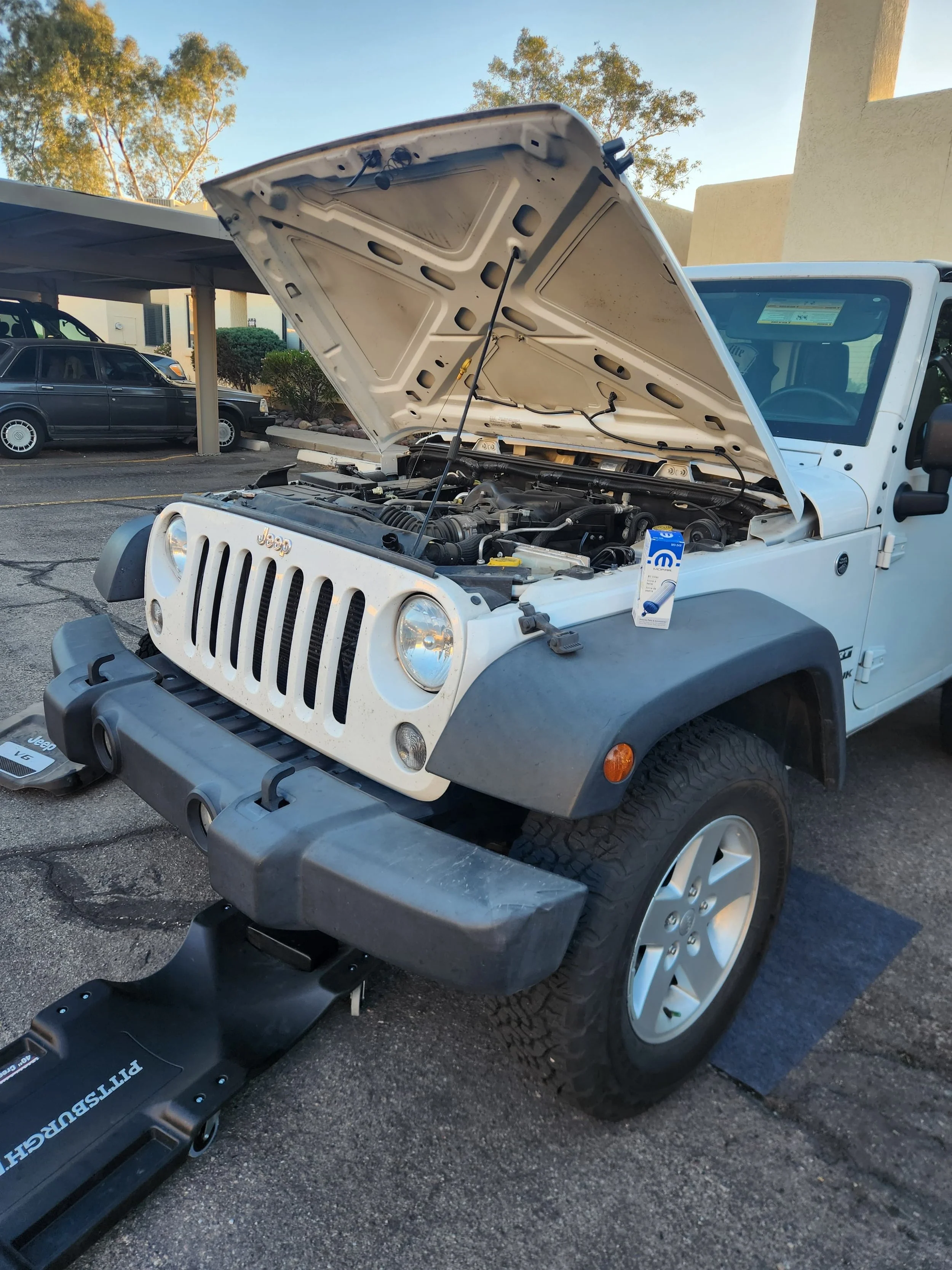 White Jeep with open hood parked in parking lot, with a troubleshooting device connected to the engine.