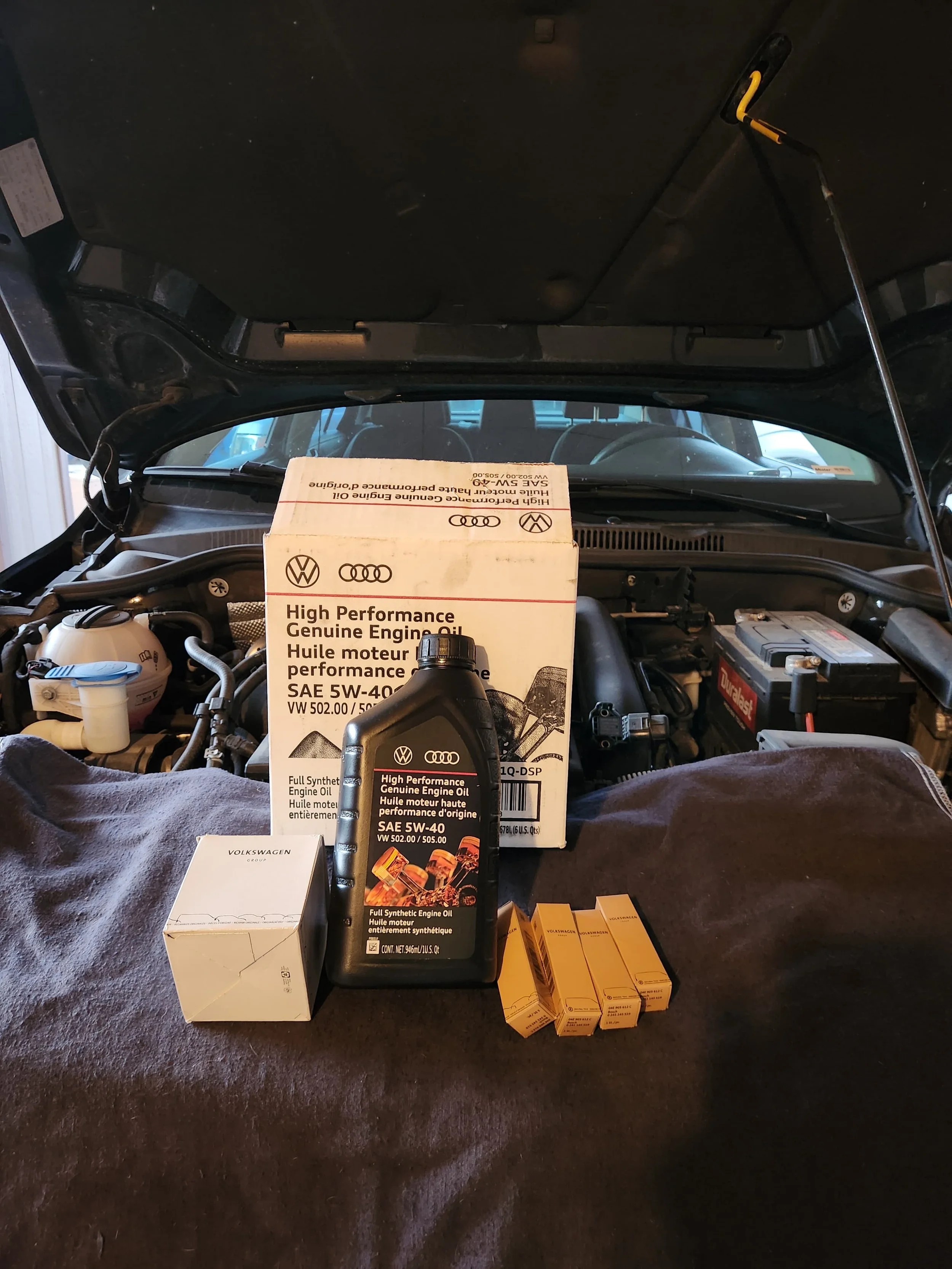 Open car hood revealing car parts and engine, with car oil and filters placed in the foreground.