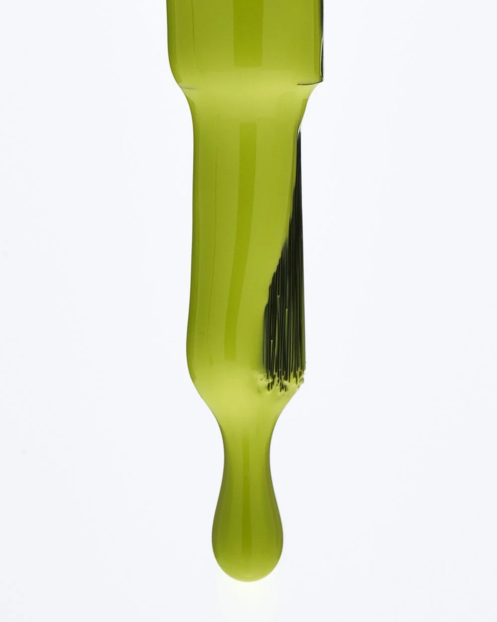 A close-up of nail polish brush with bright green paint dripping from its bristles.