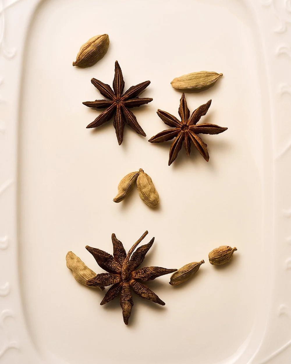 Cardamom and star anise spices arranged on a white surface.