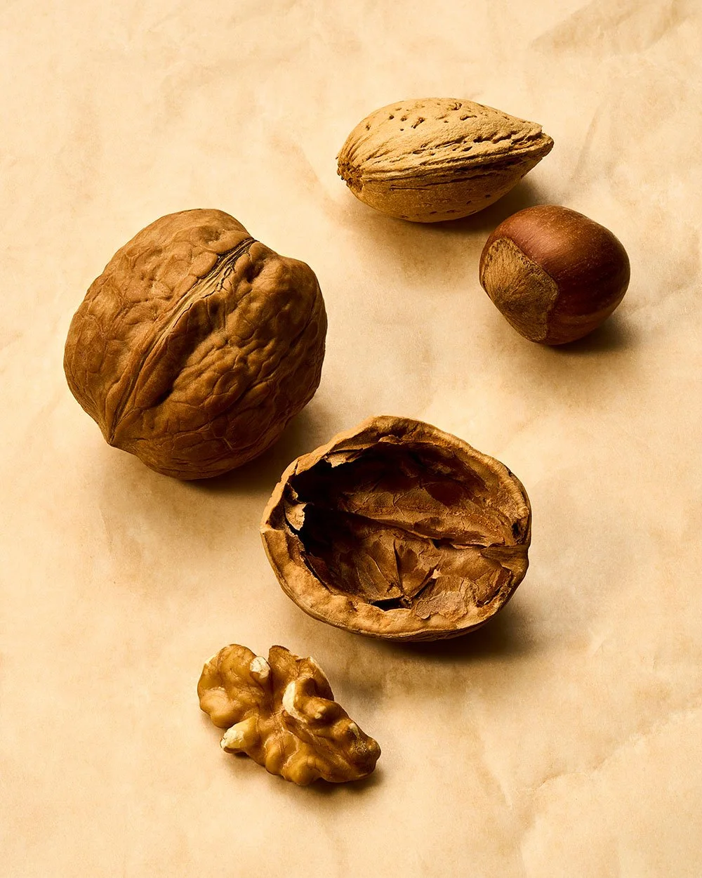 A collection of mixed nuts including a walnut, two hazelnuts, an open walnut shell with nut meat, an almond, and a walnut piece, all arranged on a light surface.