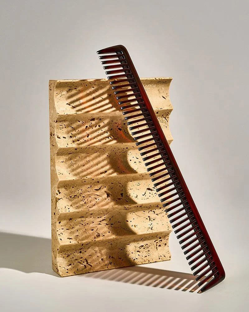 A ceramic soap dish with a black and red comb resting on top, casting shadows on the soap dish.