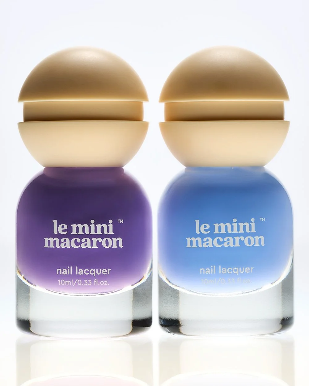 Two bottles of le mini macaron nail lacquer, one purple and one blue, with rounded caps resembling macaron shells