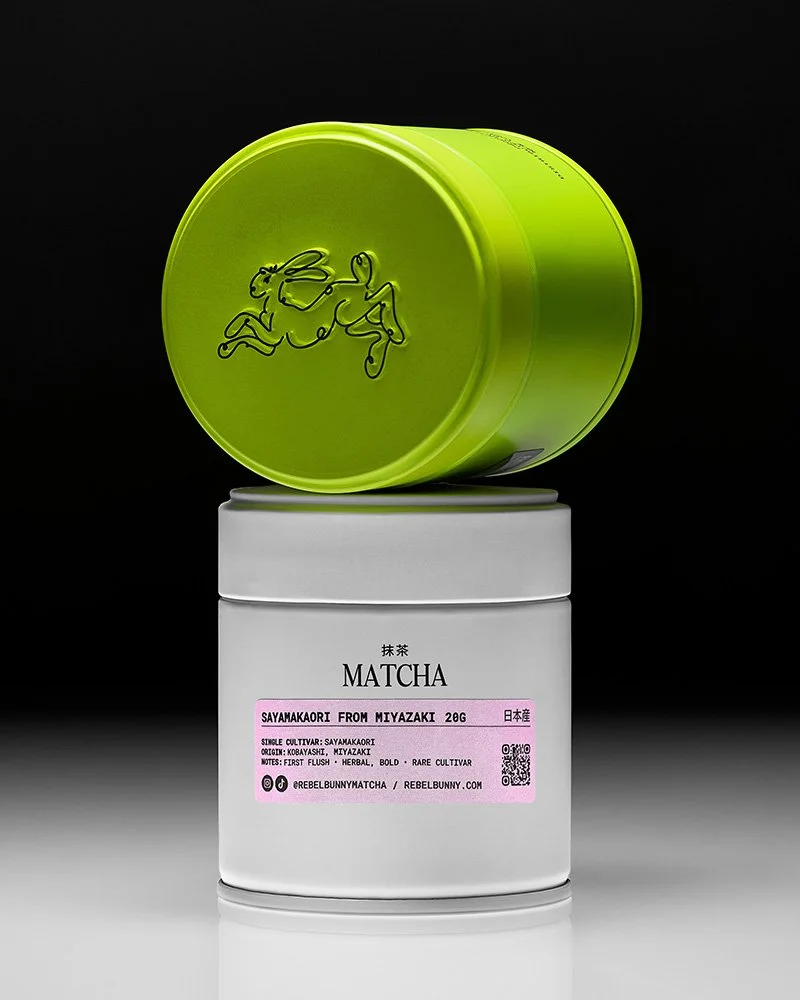 A container of matcha tea powder with green lid and a white jar labeled 'MATCHA' and 'SAYAMAKAOIRI FROM MIYAZAKI 20G' against a black background.