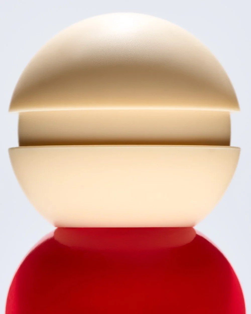 Close-up of a cap and bottle of red le mini macaroni nail lacquer on a reflective surface with colorful blurred bottles in the background.