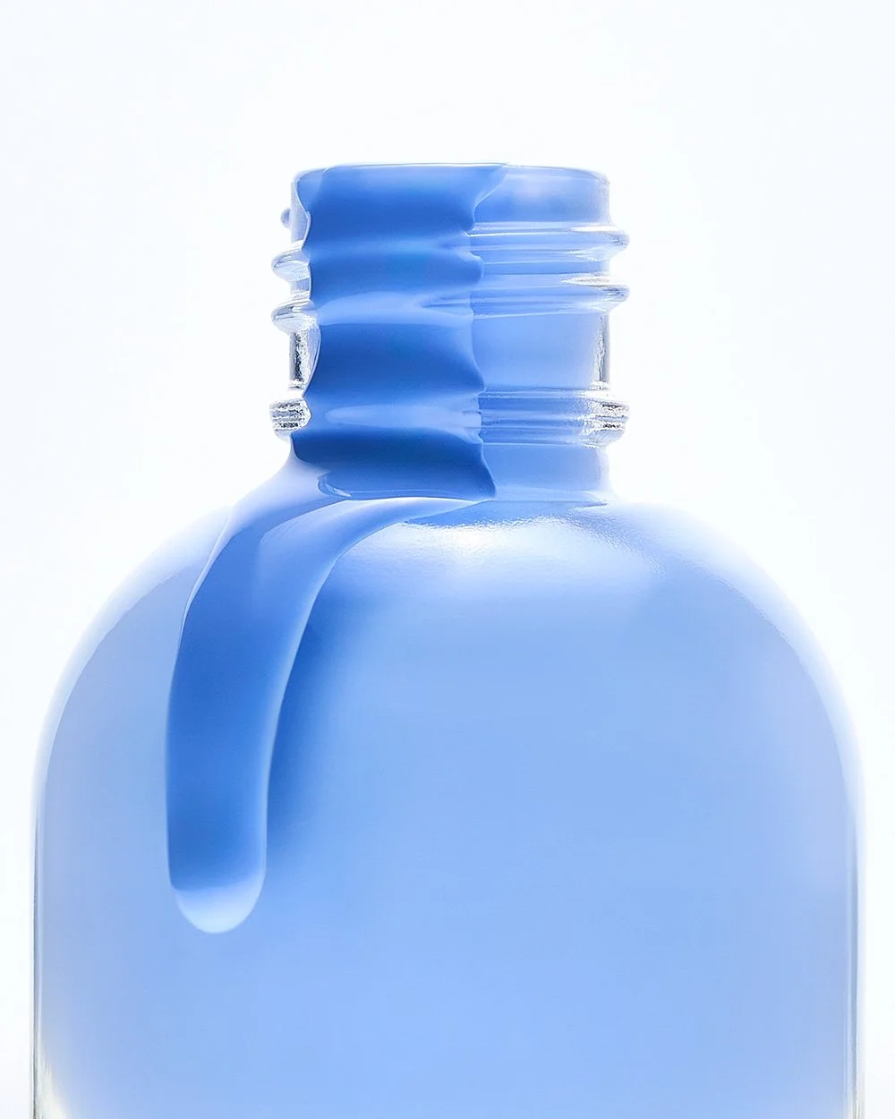 Close-up of a blue medicine or supplement bottle with a cap, with a blob of blue liquid spilling over the side.