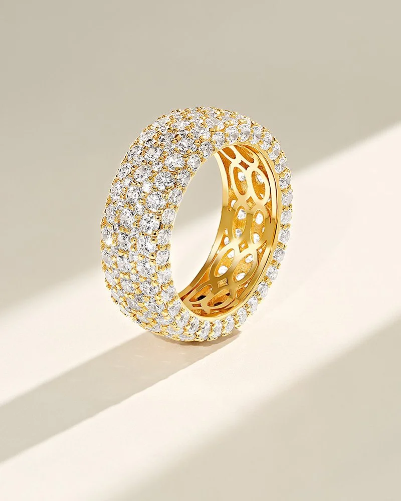 Gold ring encrusted with numerous diamonds, shown against a plain background with a shadow cast to the side.