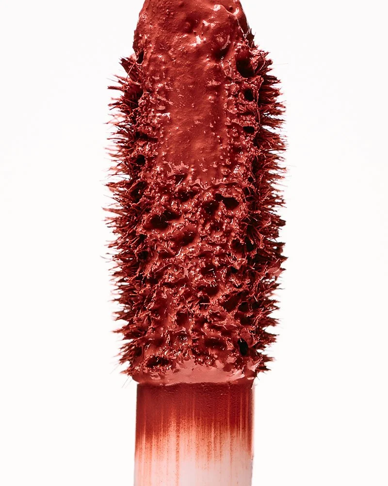 A close-up of a red liquid lipstick applicator set against a white background.