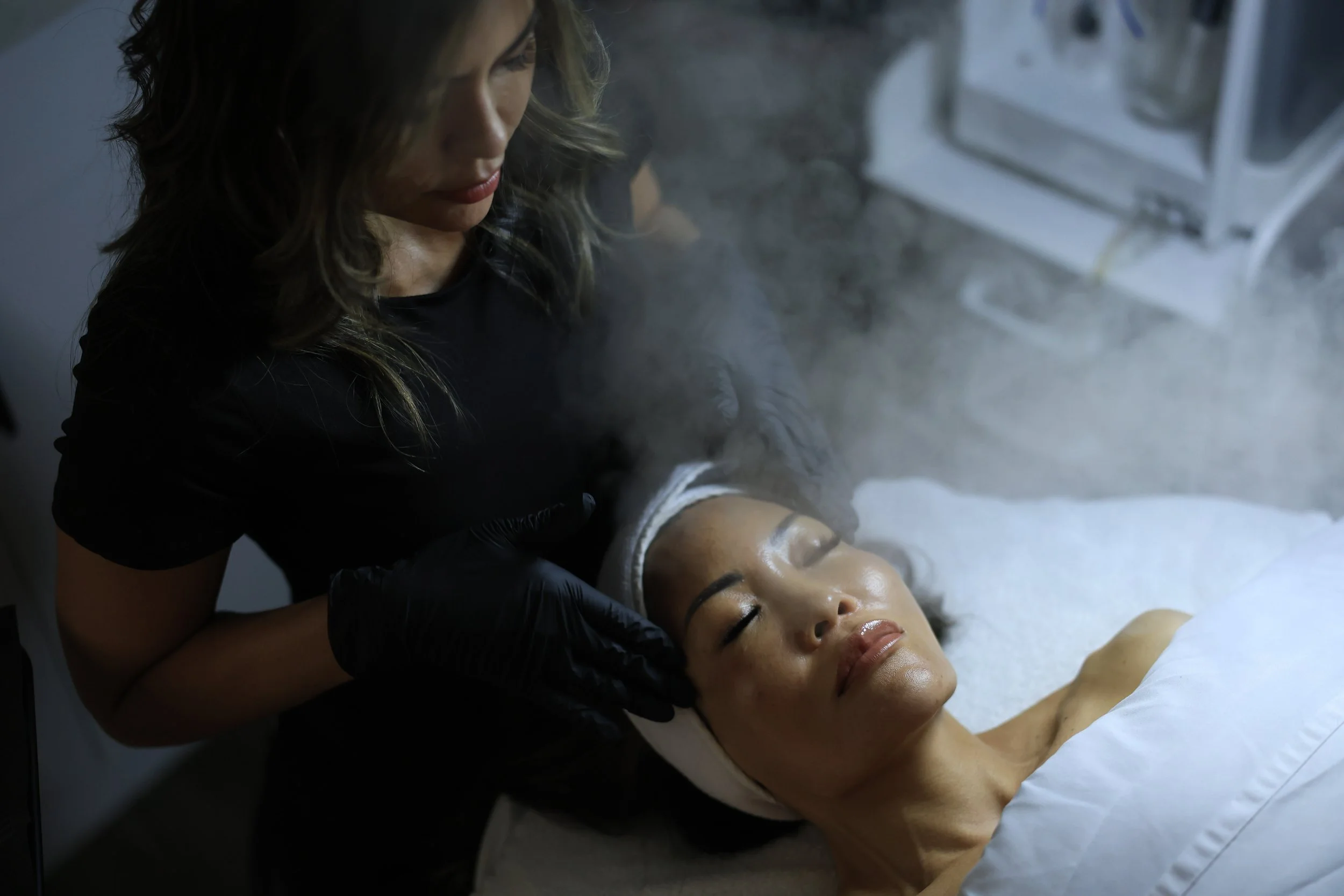 Woman laying in a relaxing spa while getting a steam facial by an aesthetician