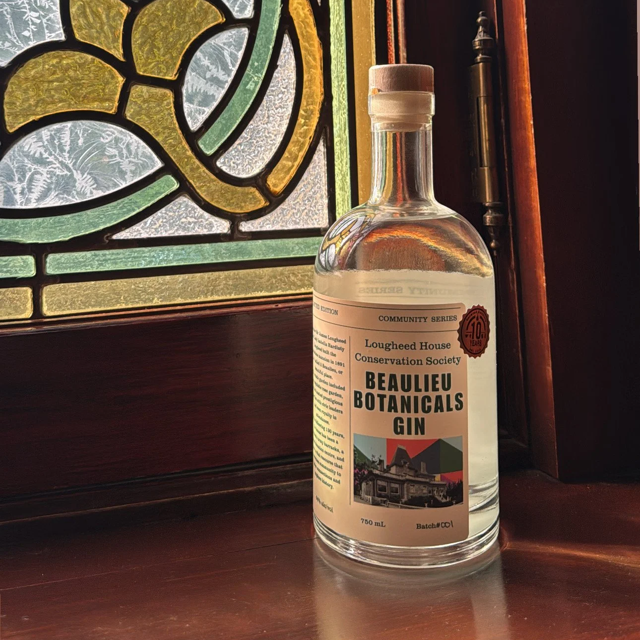 Image of a bottle of clear gin labelled "Beaulieu Botanicals Gin" in front of a stained glass window.