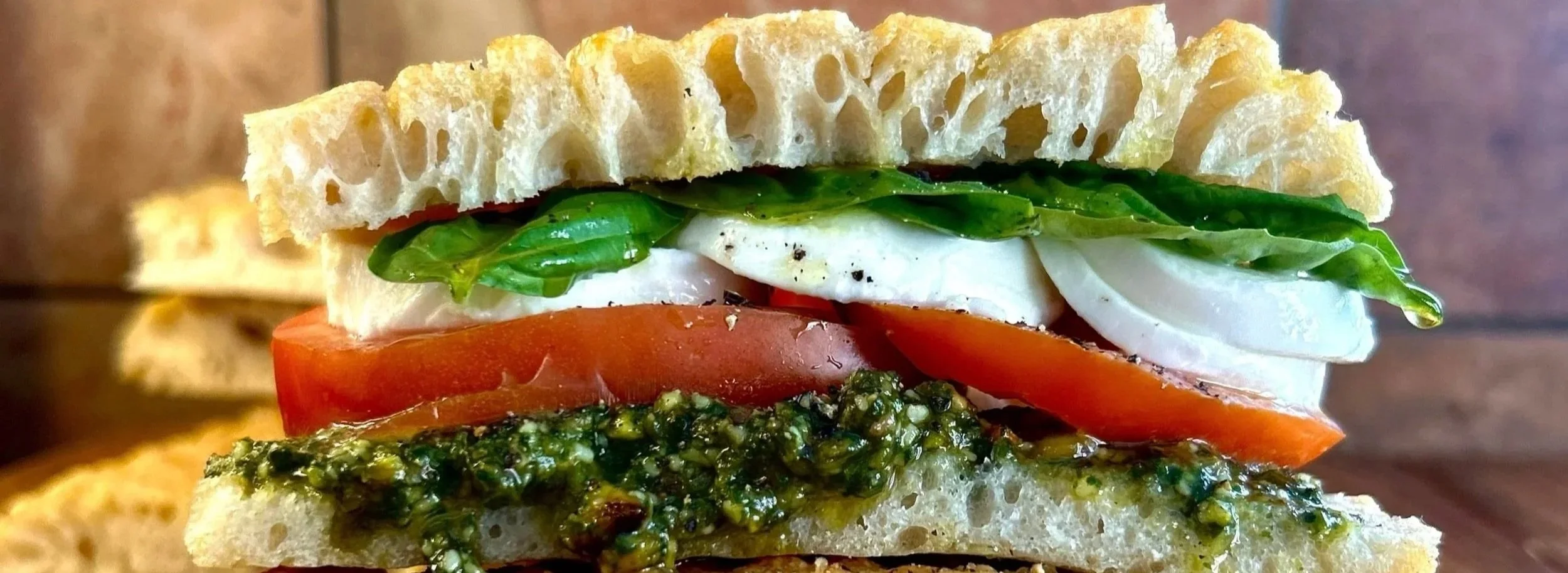 LUNCH Sandwich Shop fresh, authentic Italian sandwich with pieces of fresh basil, tomato, fresh mozzarella cheese, and pistachio basil pesto spread on fresh baked Italian schiacciata bread.