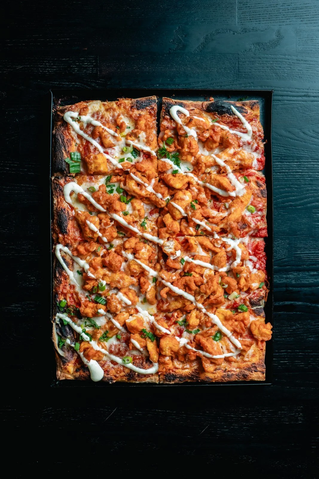 Buffalo Chicken Roman-style pizza with a creamy drizzle, photographed overhead.