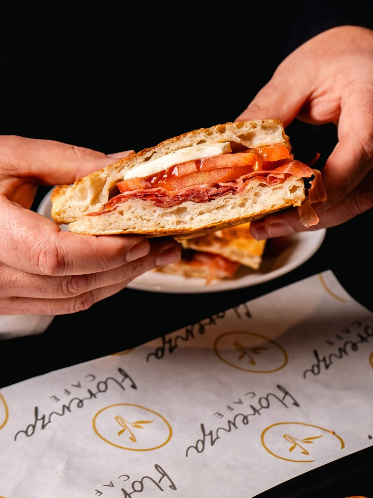 Hands holding a cut panini above Florenza-branded serving paper.