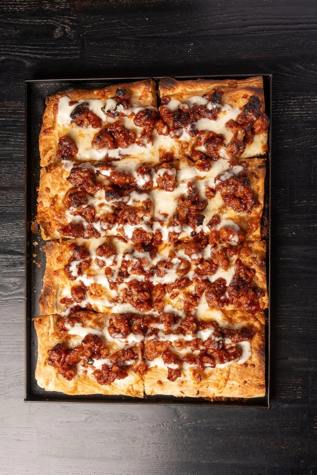 Rectangular Roman-style pizza with golden melted cheese and browned toppings, photographed overhead.