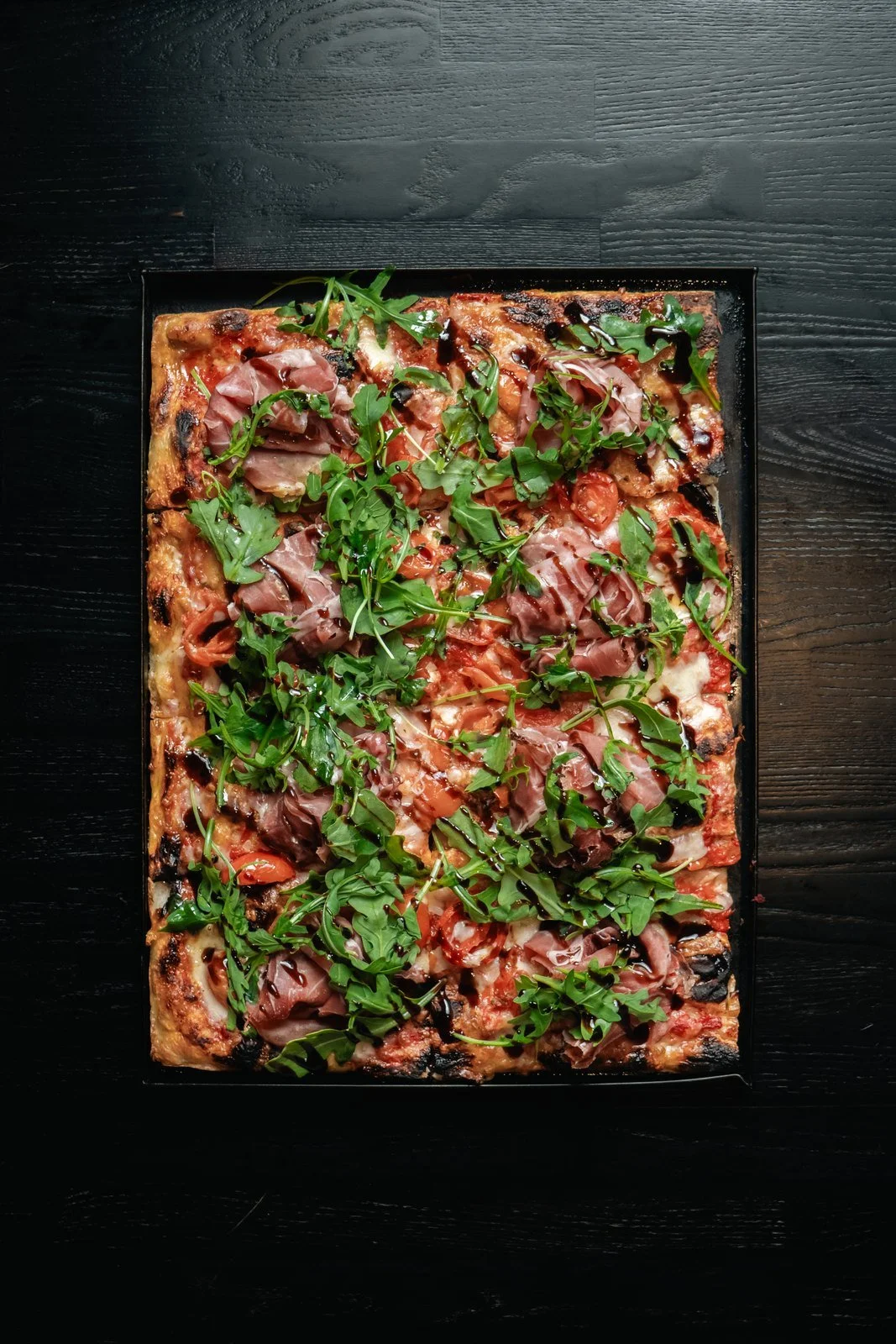 Baba Roman-style pizza with prosciutto, arugula, cherry tomatoes, and balsamic glaze.
