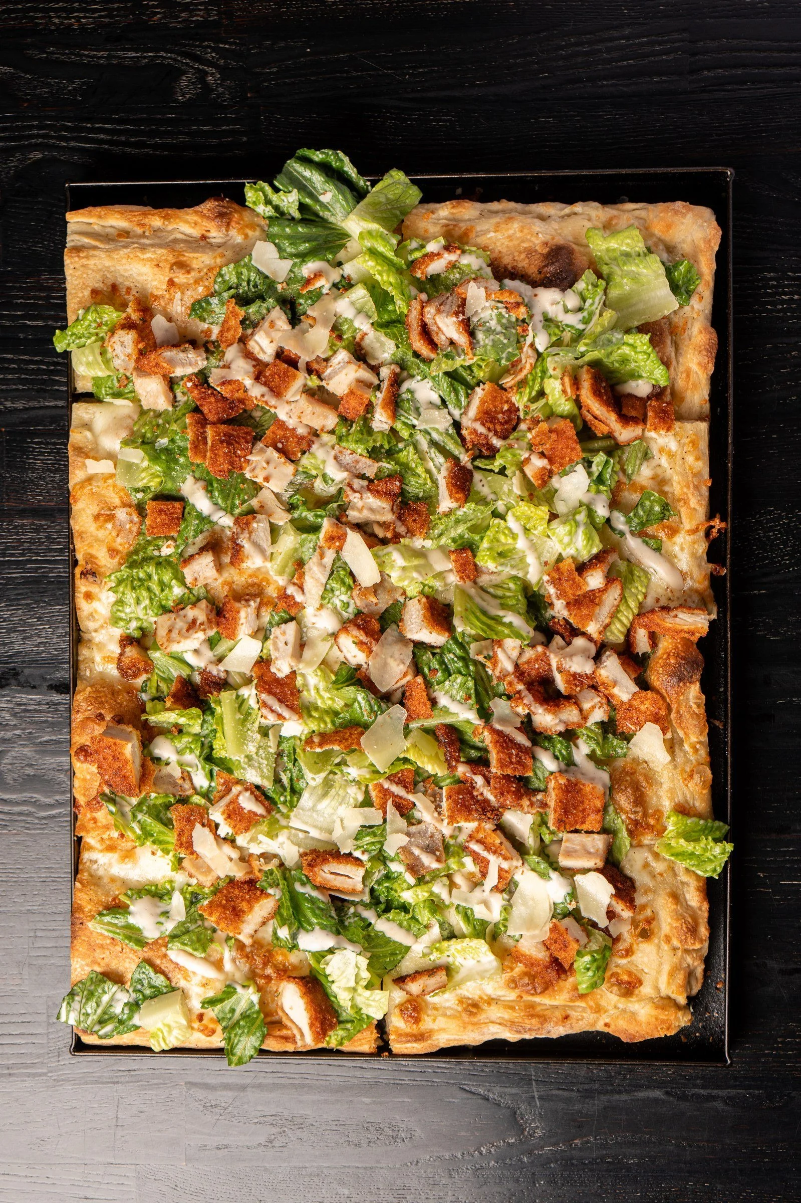 Chicken Caesar Roman-style pizza topped with chicken and crisp salad greens.