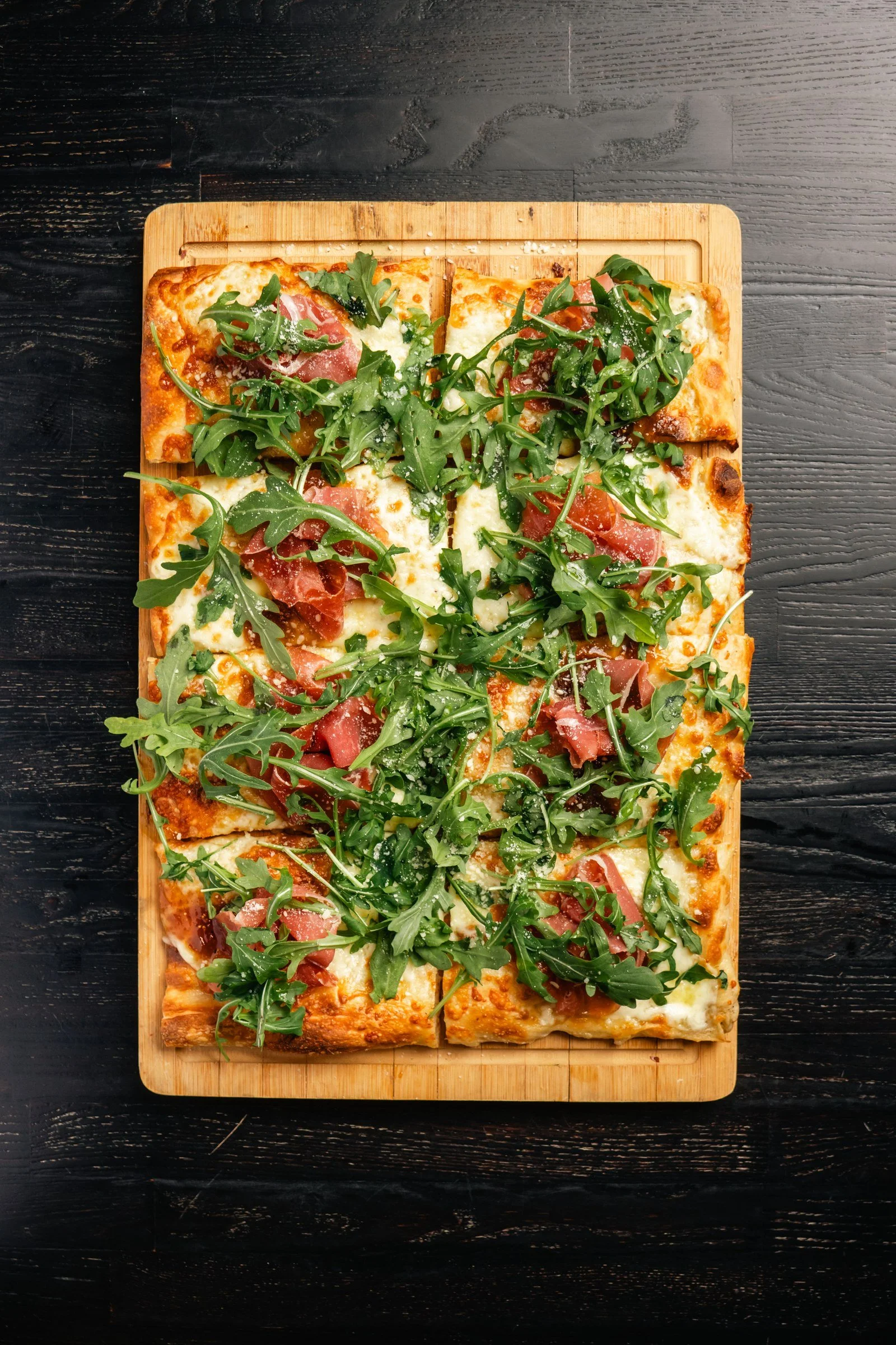 Prosciutto and fig Roman-style pizza topped with arugula, photographed overhead.