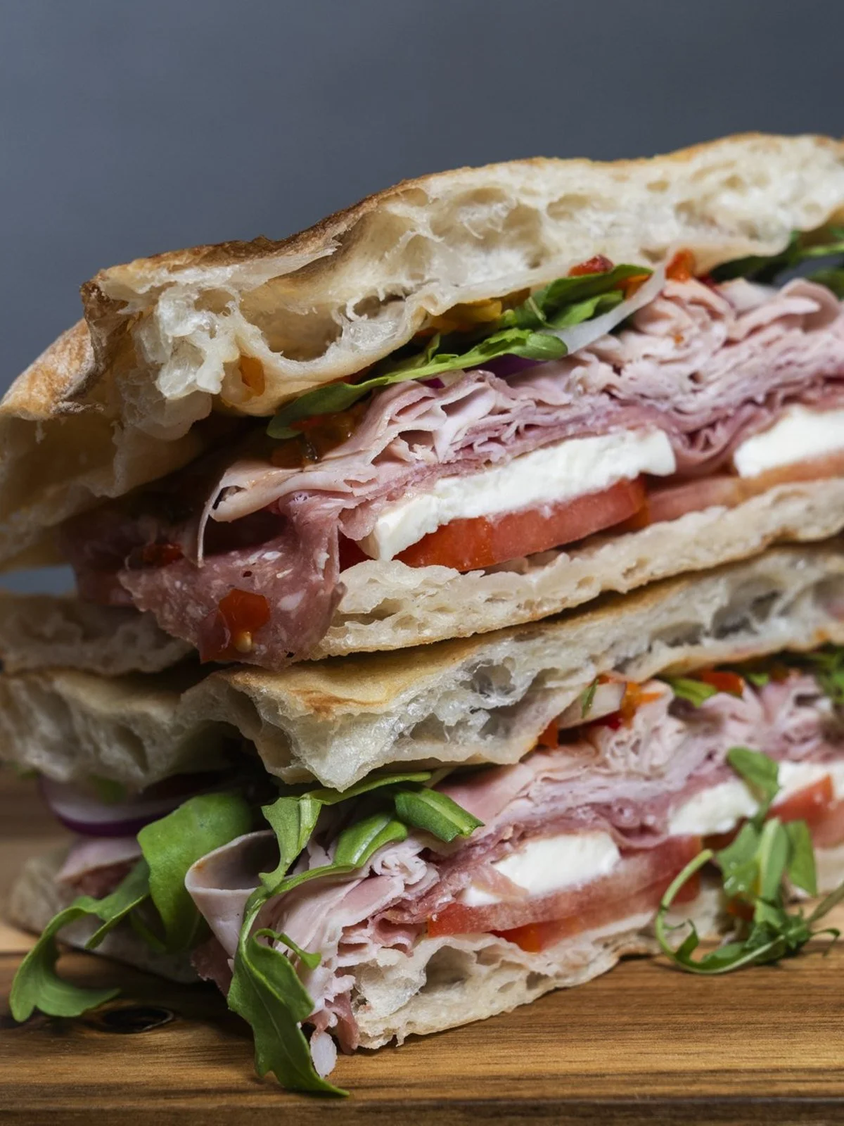 Stacked panini showing airy bread, sliced meat, cheese, tomato, and greens.