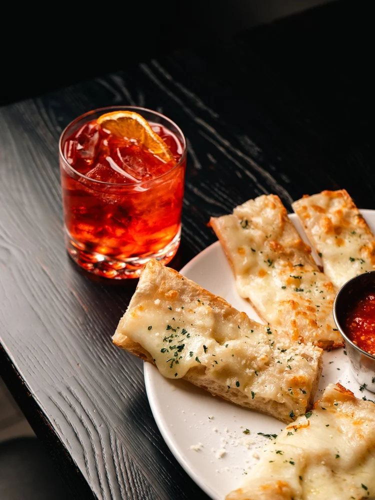 A Negroni beside cheese bread and dipping sauce at Florenza