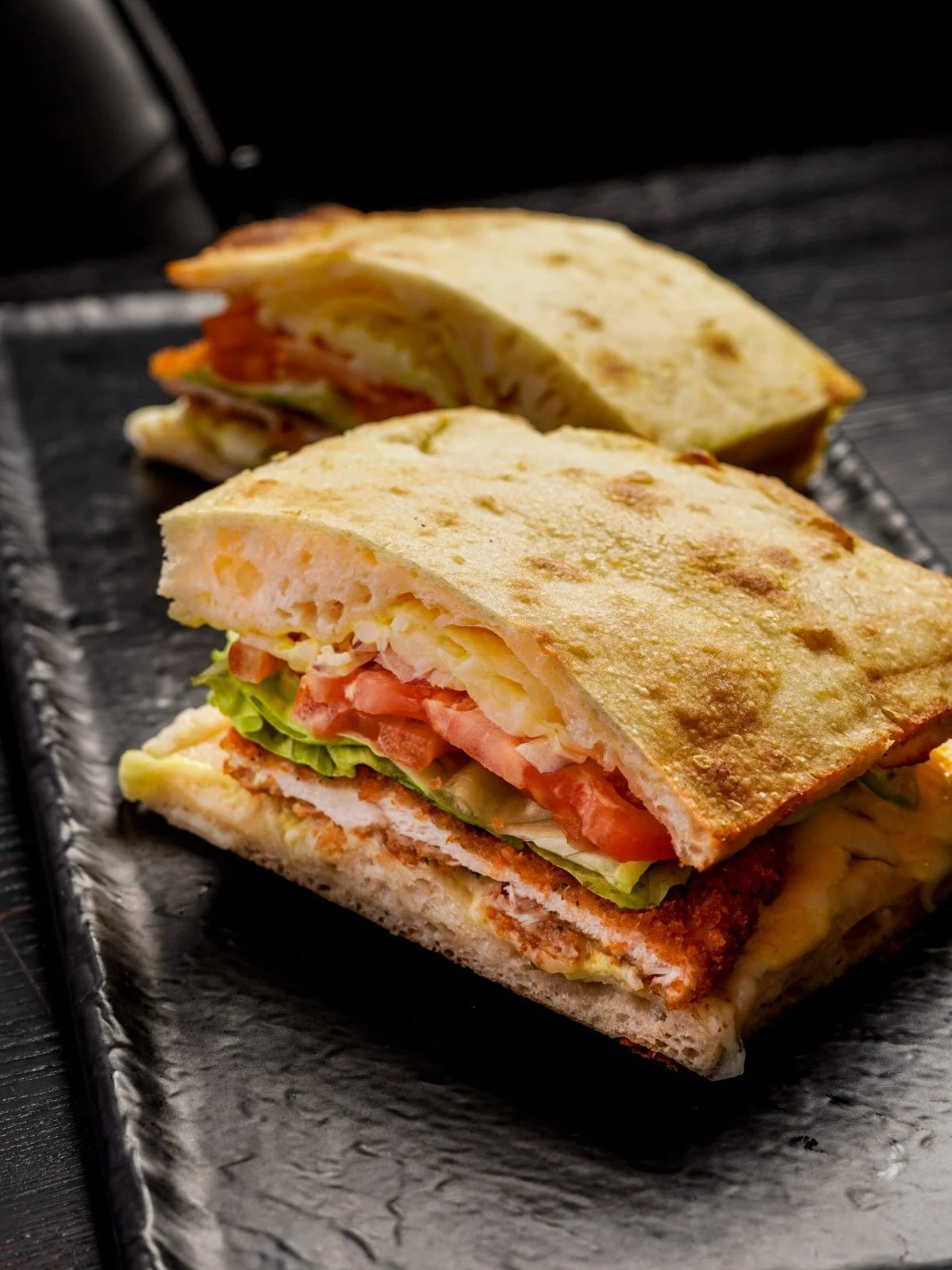Cut chicken panini showing crisp bread, chicken cutlet, tomato, and greens.