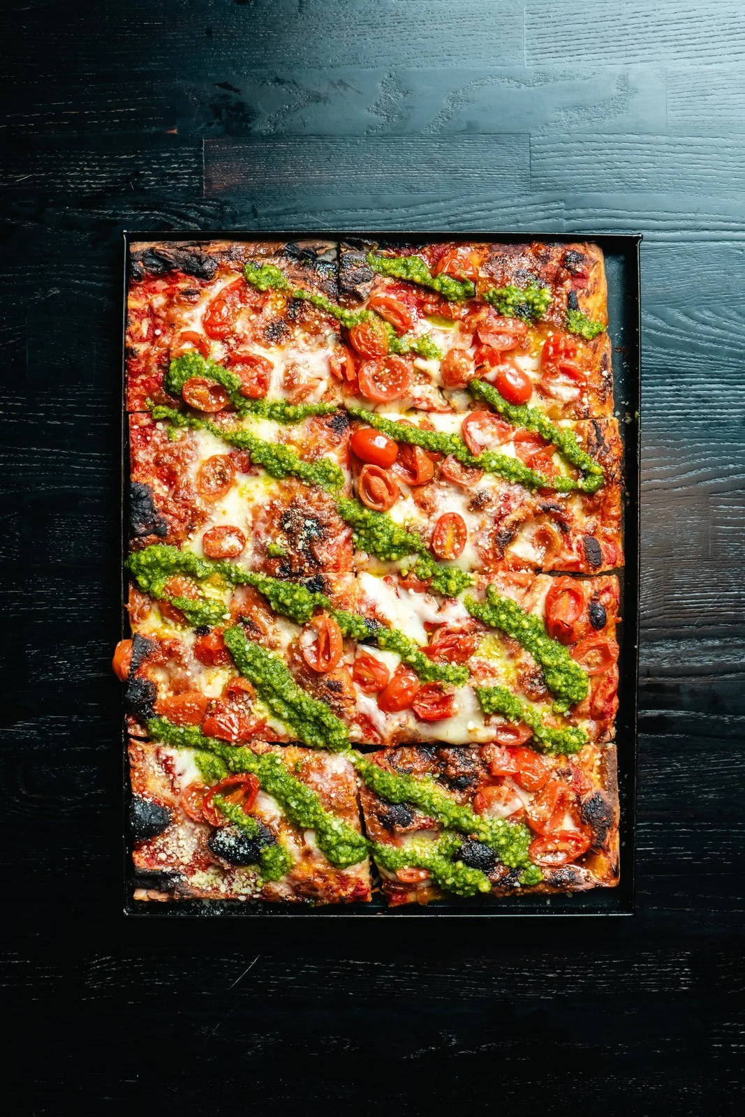 Caprese Roman-style pizza with cherry tomatoes, mozzarella, basil, and pesto.