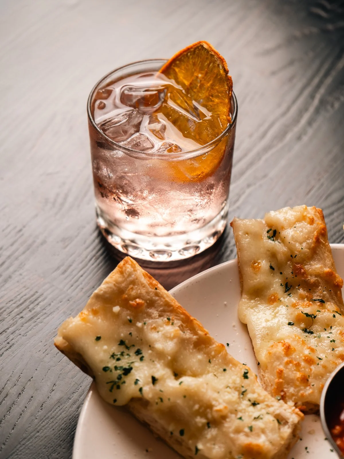 Cocktail with a dried orange slice beside Roman-style pizza strips