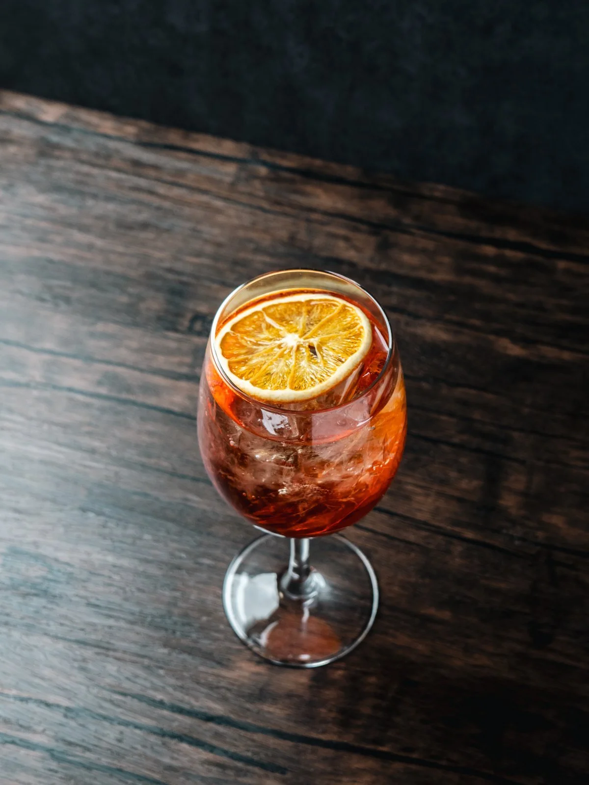 Aperol Spritz in a stemmed glass with a dried orange slice, on a dark wood table at Florenza