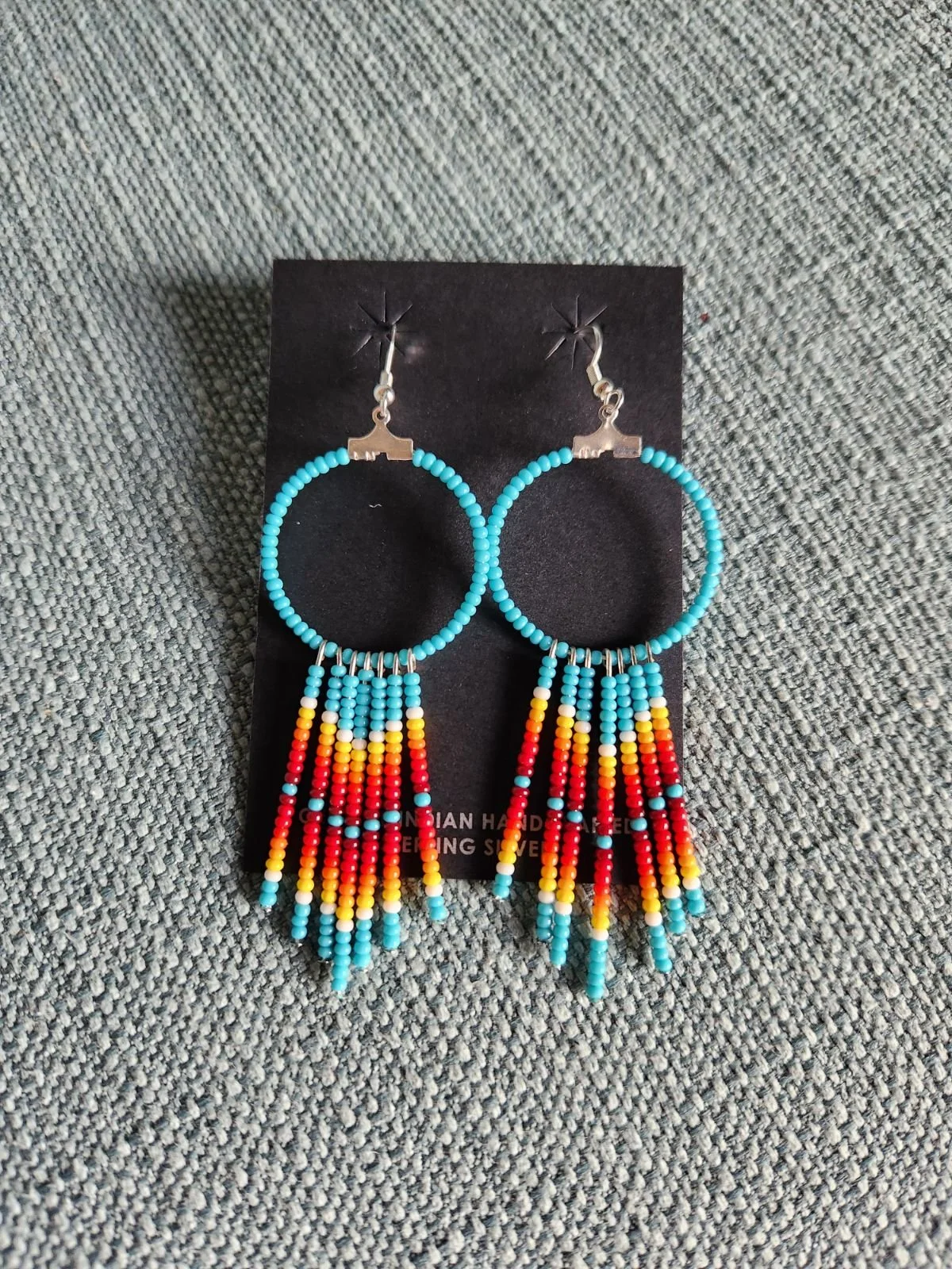 Colorful beaded earrings with small turquoise, red, yellow, and orange beads and silver accents, hanging on a black display card.
