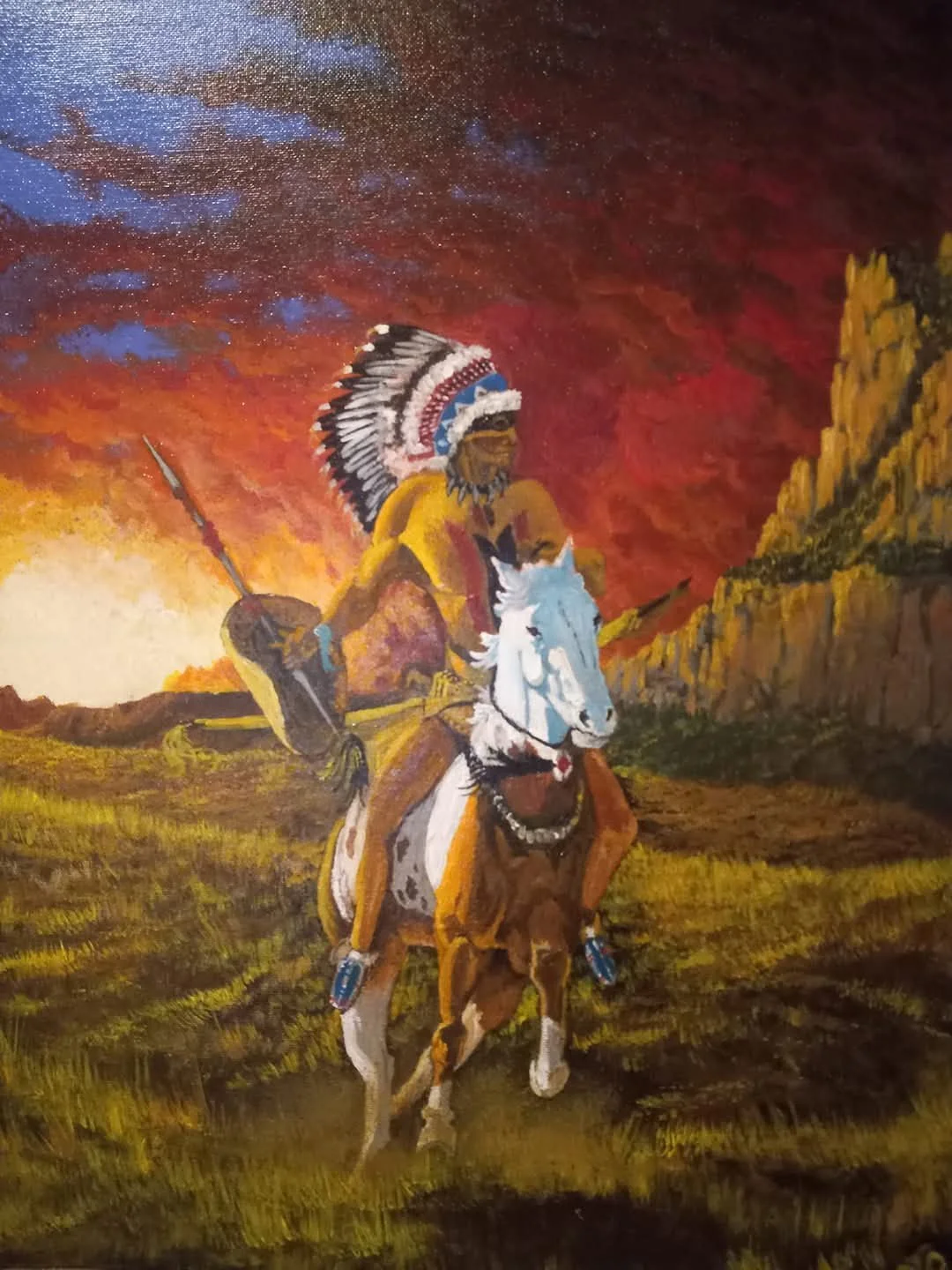 A vibrant painting of a Native American warrior riding a white horse, wearing a feathered headdress and holding a spear, with a sunset sky and mountains in the background.