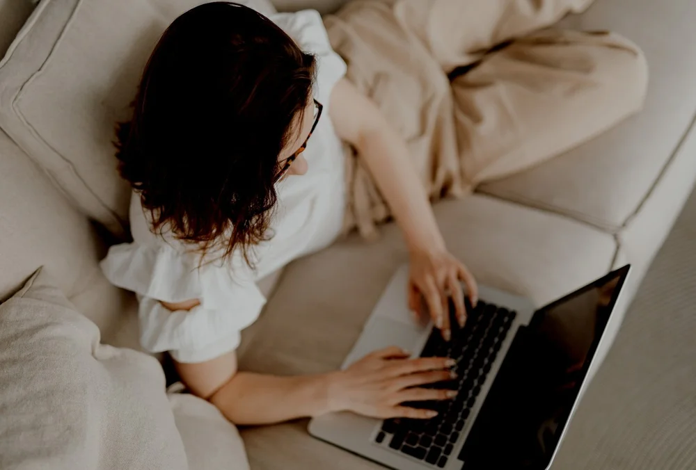 Woman sitting on a sofa at home reading on a laptop