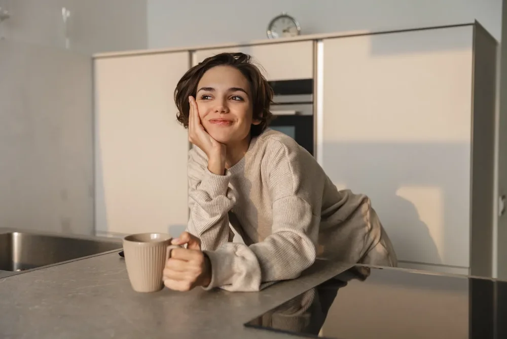 Woman resting her chin on her hand at a kitchen counter, looking calm
