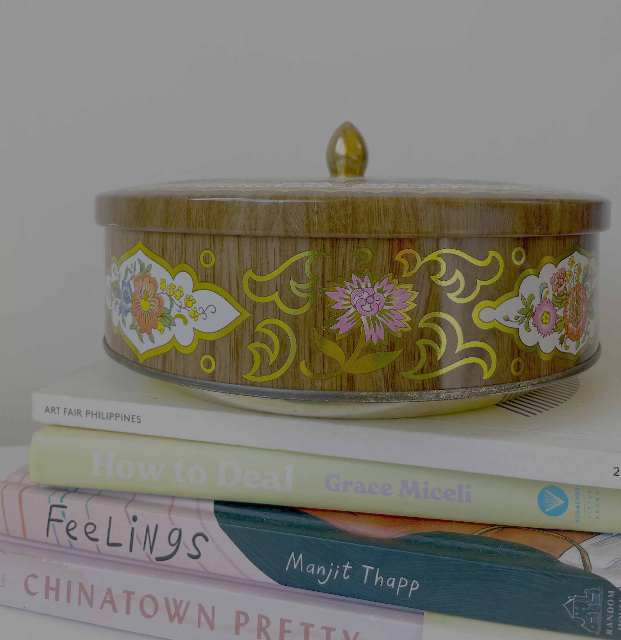 Close-up of a decorated container with a gold lid on a white background. The container has colorful floral patterns and appears to be part of an art fair display, with visible text mentioning the Philippines and an artist named Grace Miceli.