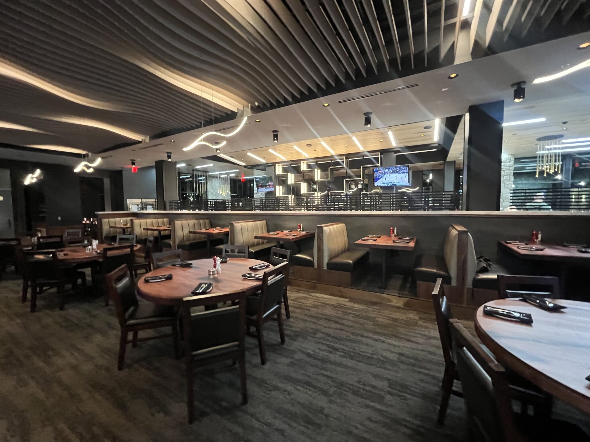 Stoney River Restaurant in Madison, Alabama. Interior dinning room with wave featured ceiling and lights mimicking water. stylish bar in the back. Tables, chairs, and booths in front