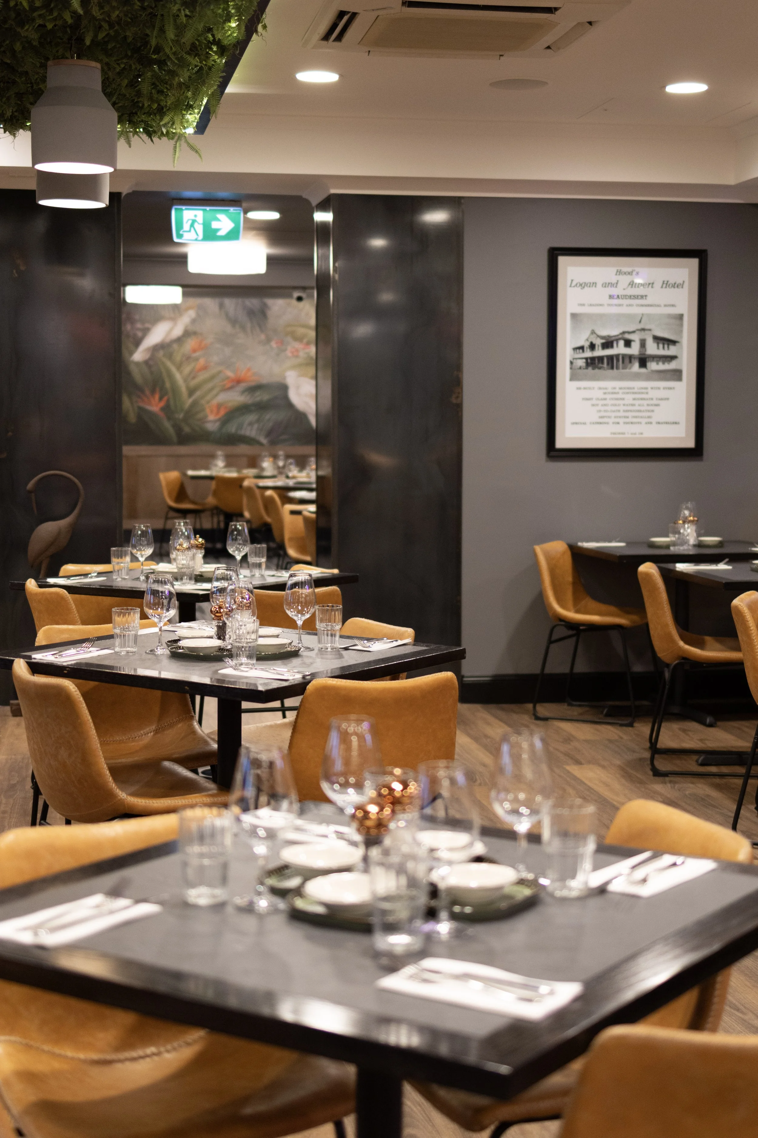 Interior of a restaurant with tables set for dining, including plates, glasses, and silverware, with warm lighting and modern decor.