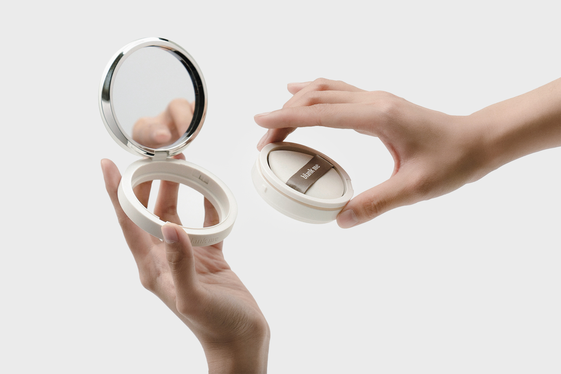 Two hands holding an open Blank Me Halo compact, showing the mirror and cushion insert