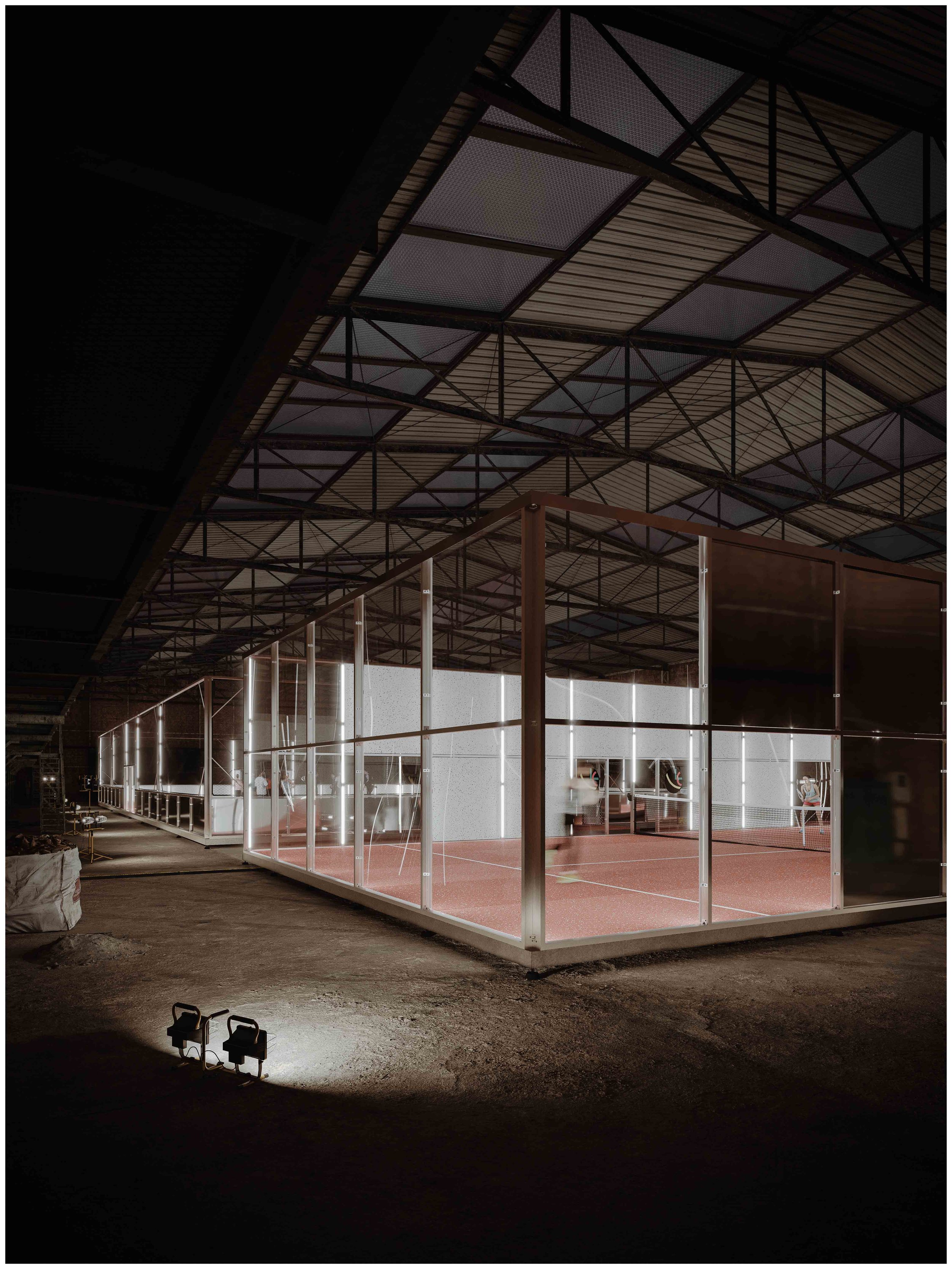 Vue d'une salle de padel, conçue pour le badminton, avec des murs en verre, un sol en tapis rouge et des joueurs en action.