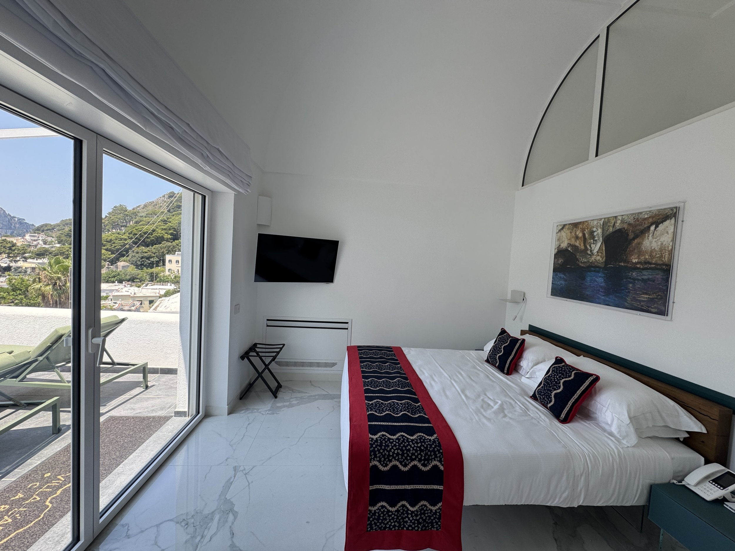 White bedroom with large windows, blue curtains, and a flat-screen TV on the wall