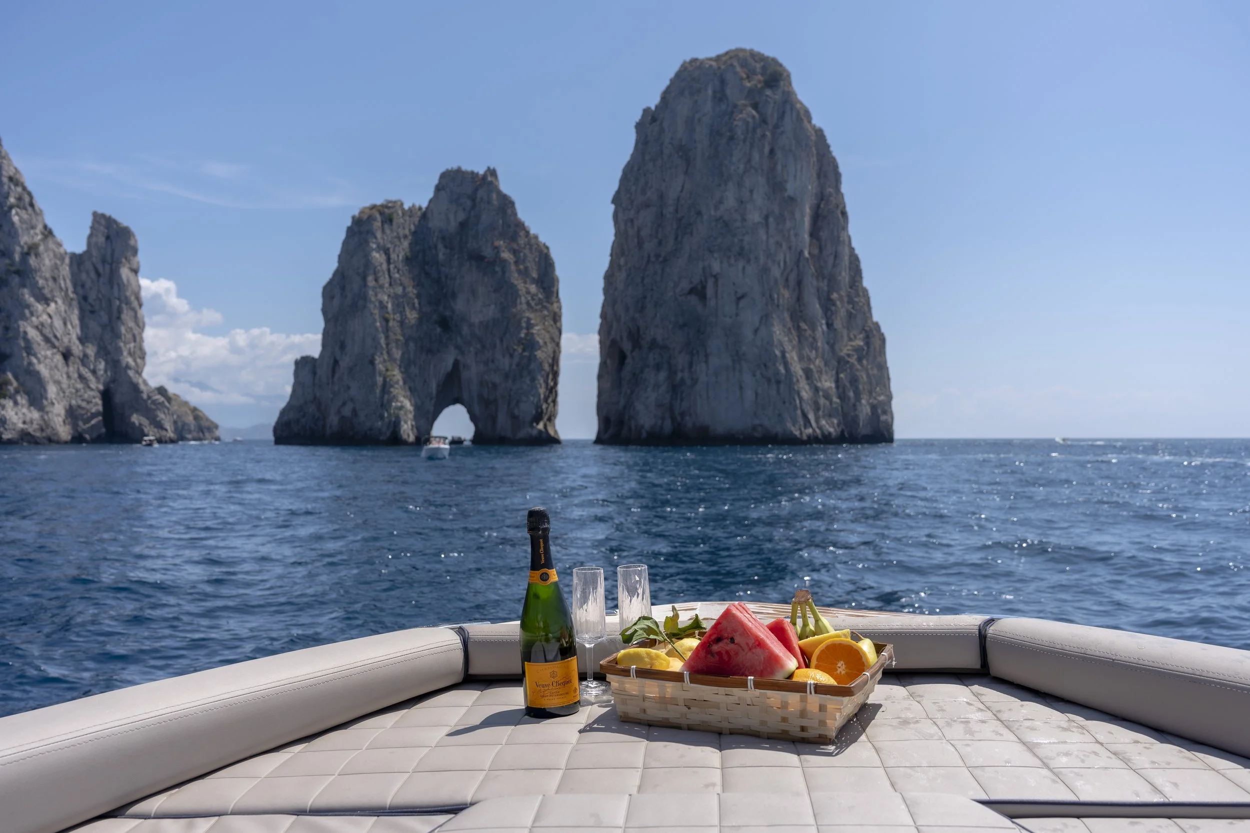 Fresh fruit and champagne set on the bow of a boat, overlooking the iconic Faraglioni Rocks in Capri, with stunning views of the Mediterranean Sea.
