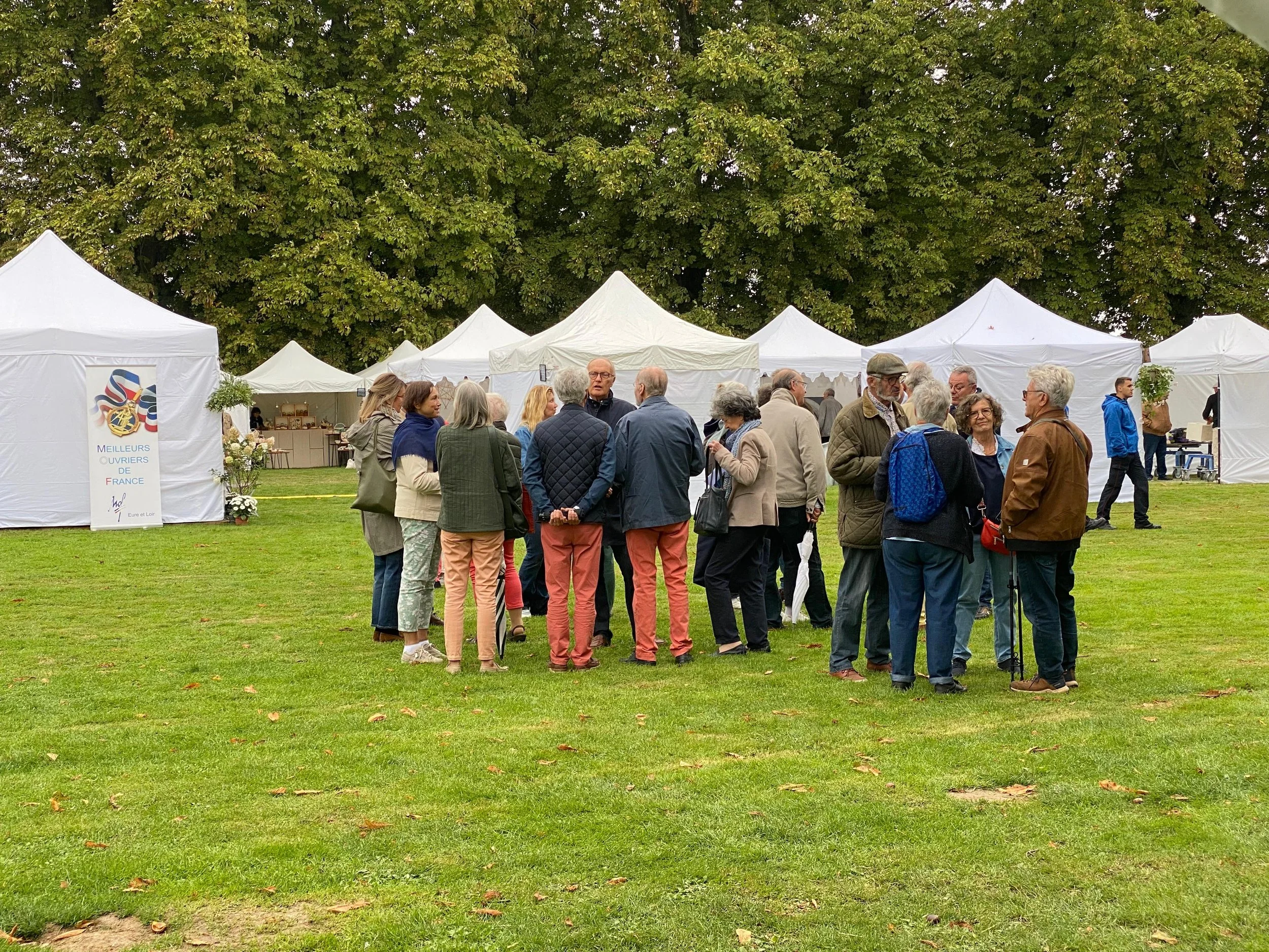 Groupe de personnes rassemblées dans un espace vert lors d'un événement, avec plusieurs tentes blanches derrière elles.