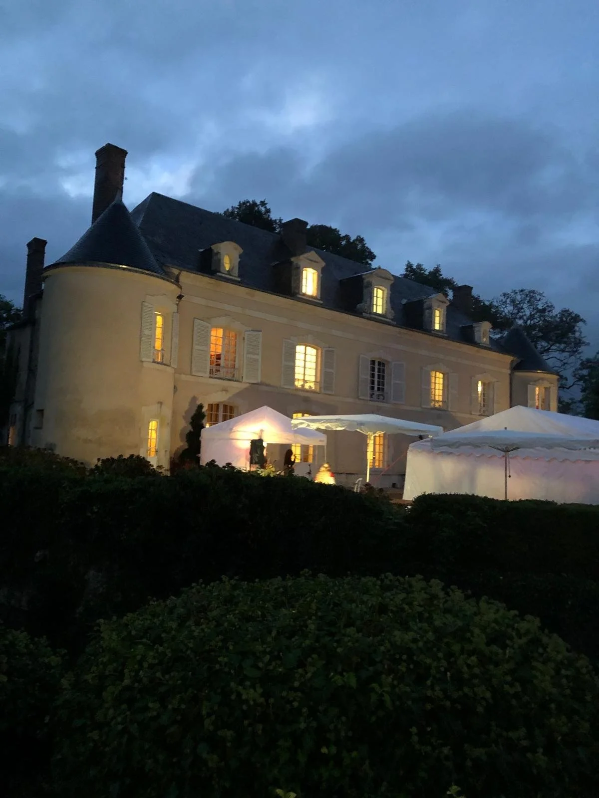 Un vieux château avec des fenêtres éclairées, tourné vers le ciel nocturne, avec des tentes blanches devant, probablement lors d'une soirée ou d'un événement.
