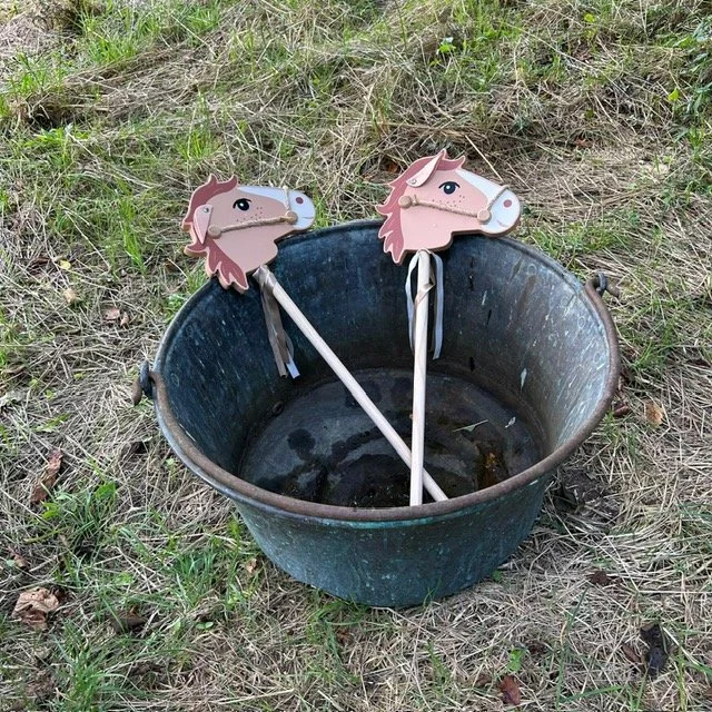 Deux baguettes avec des têtes de cheval en bois, placées dans un seau en métal en plein air.