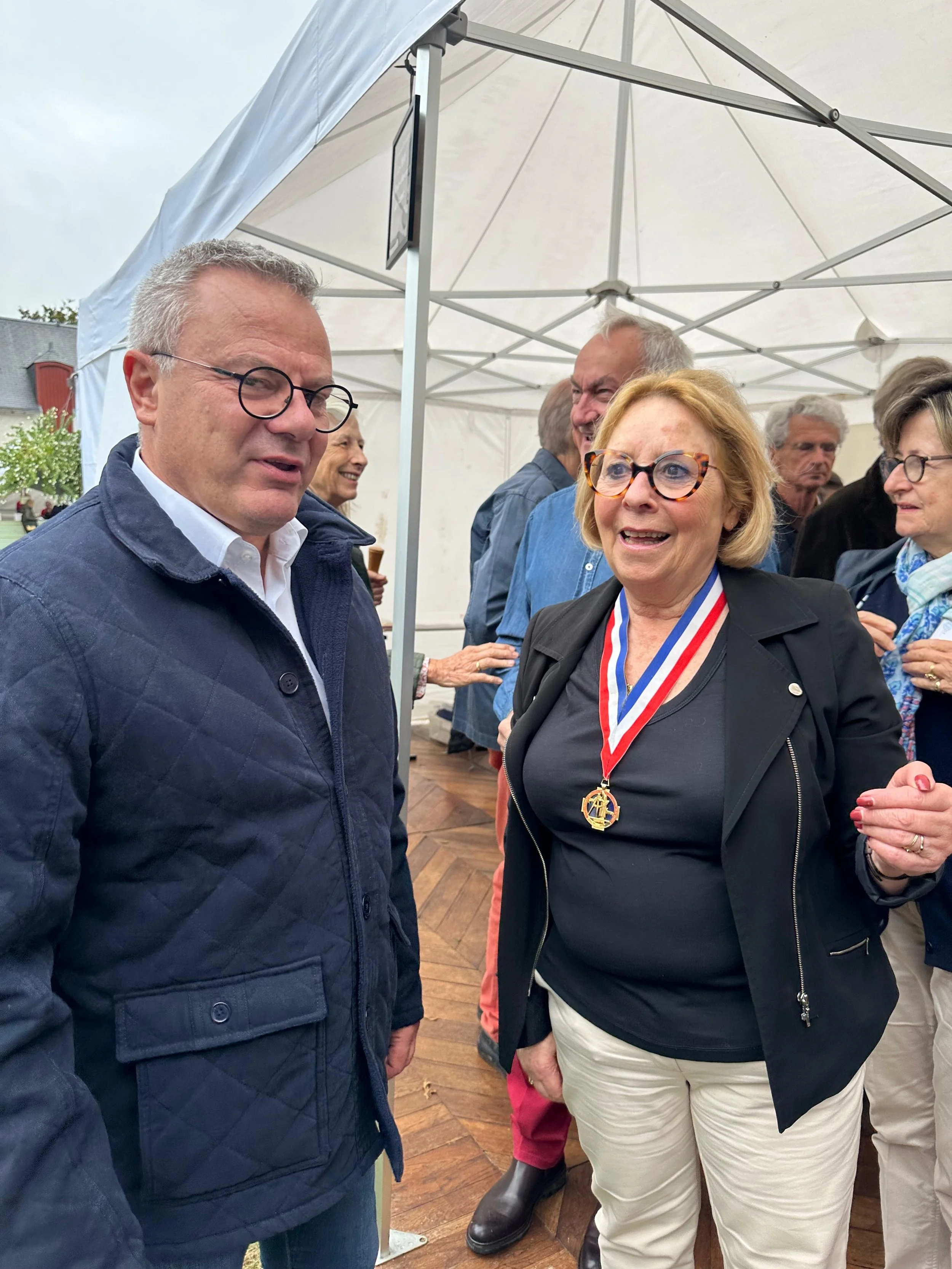 Groupe de personnes en conversation lors d'une cérémonie en extérieur, avec une femme portant une médaille.