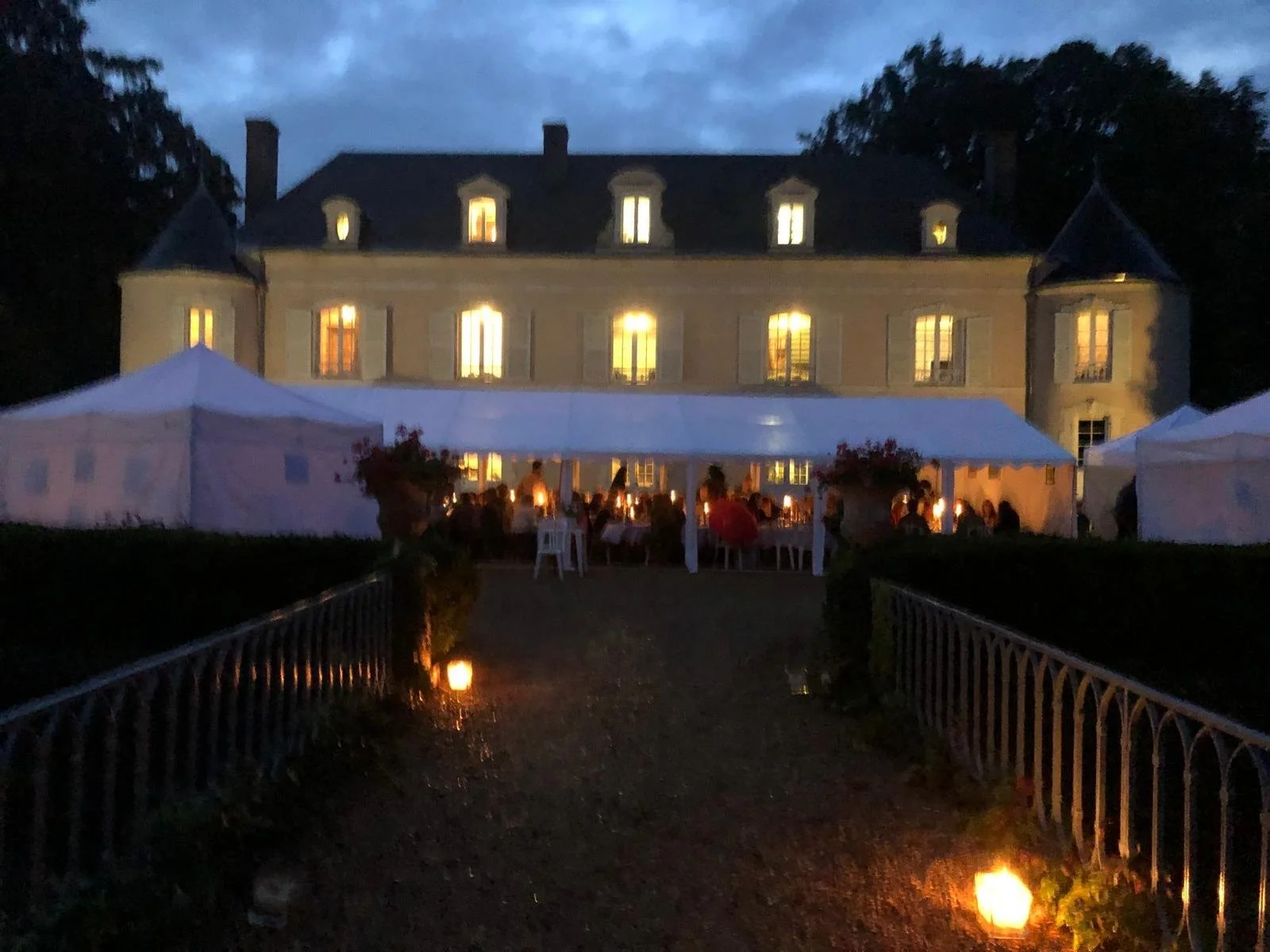 Château illuminé en soirée avec une tente blanche devant, où des personnes dînent à la lumière de lampions