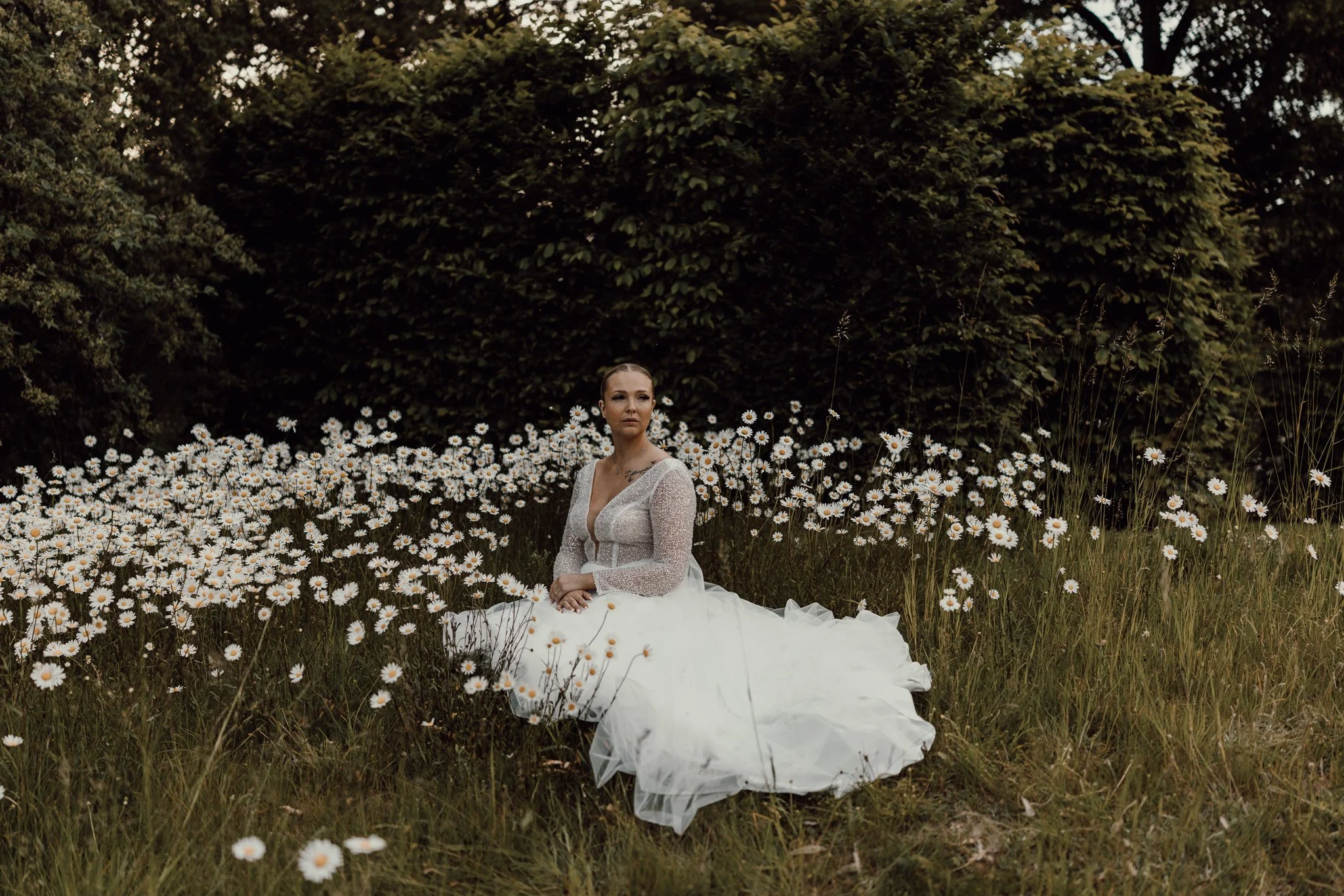 kvinna i vit brudklänning som siter i ett fält av vita blommor.