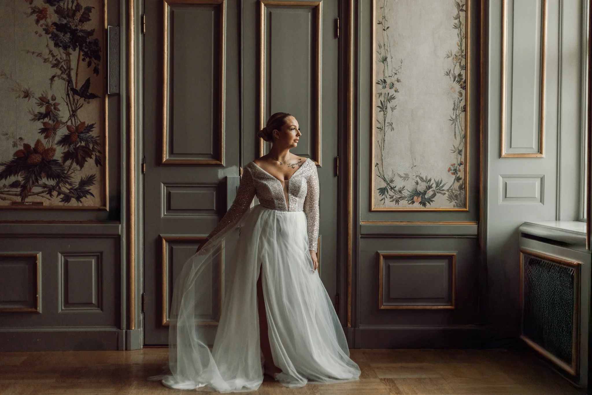 Brud står och blickar ut genom ett fönster i en stor sal på Ekolsunds slott.