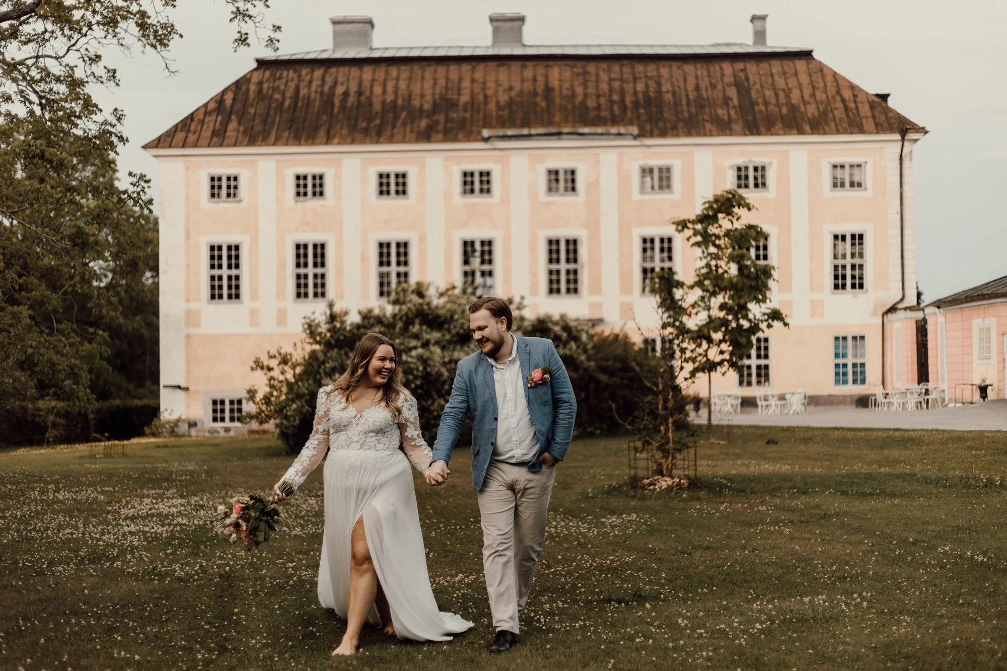 brudpar går hand i hand på en grasmatta framför Ekolsunds slott.