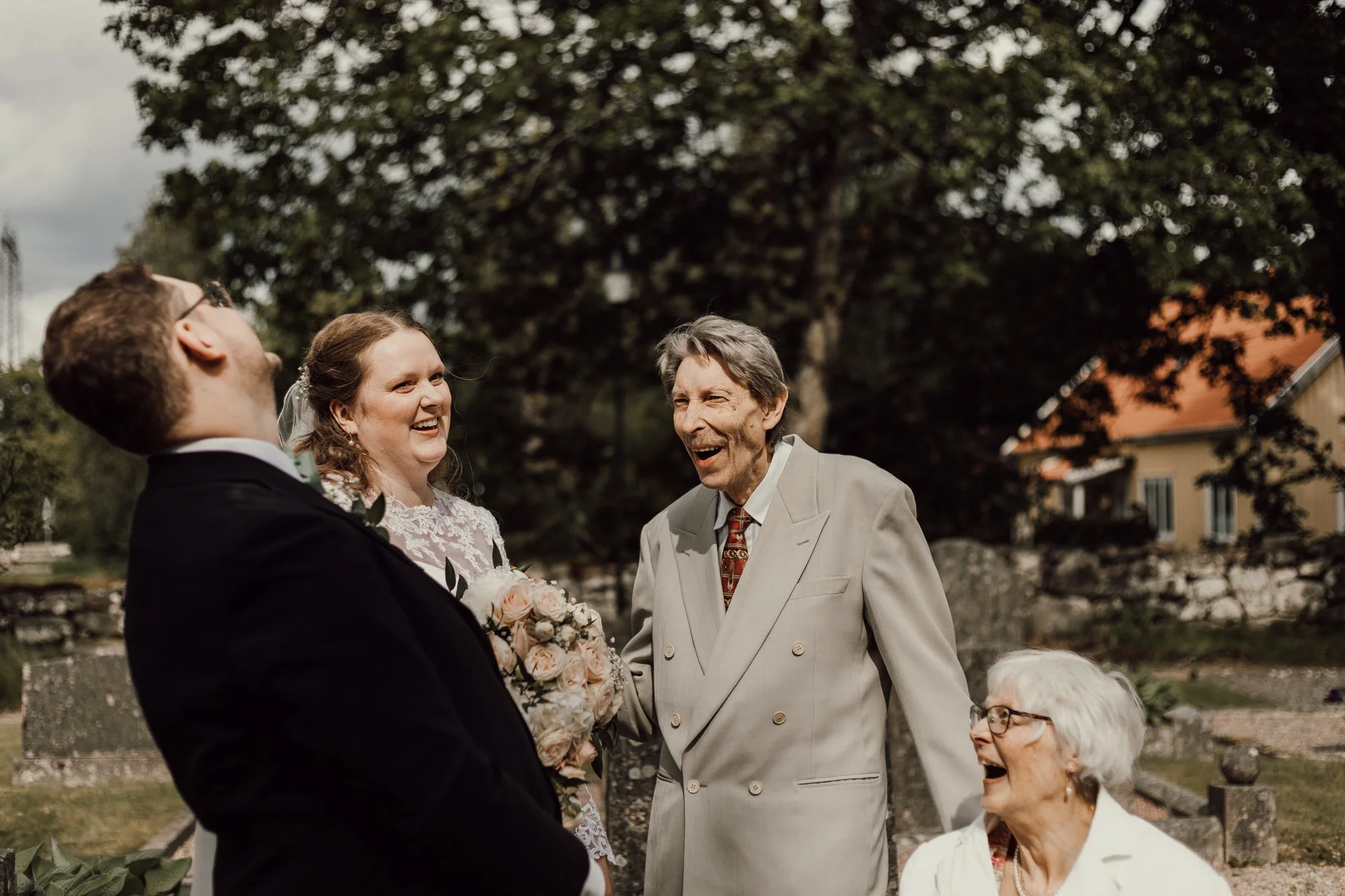 brudpar konverserar med farmor och farfar utanför kyrkan en solig dag efter vigsel.