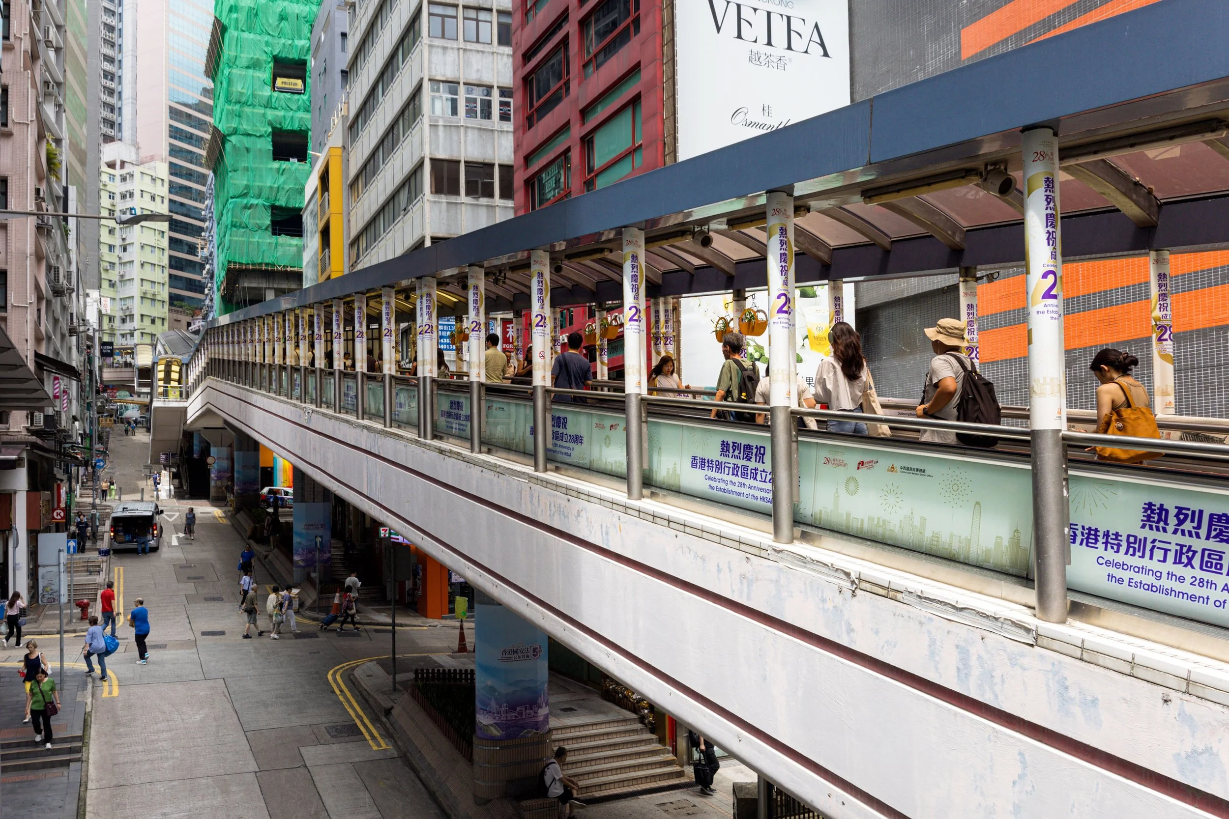 Golden sunlight streams down one of Hong Kong's lengthy escalators, creating dramatic shadows and highlights that transform the utilitarian structure into a luminous architectural feature.