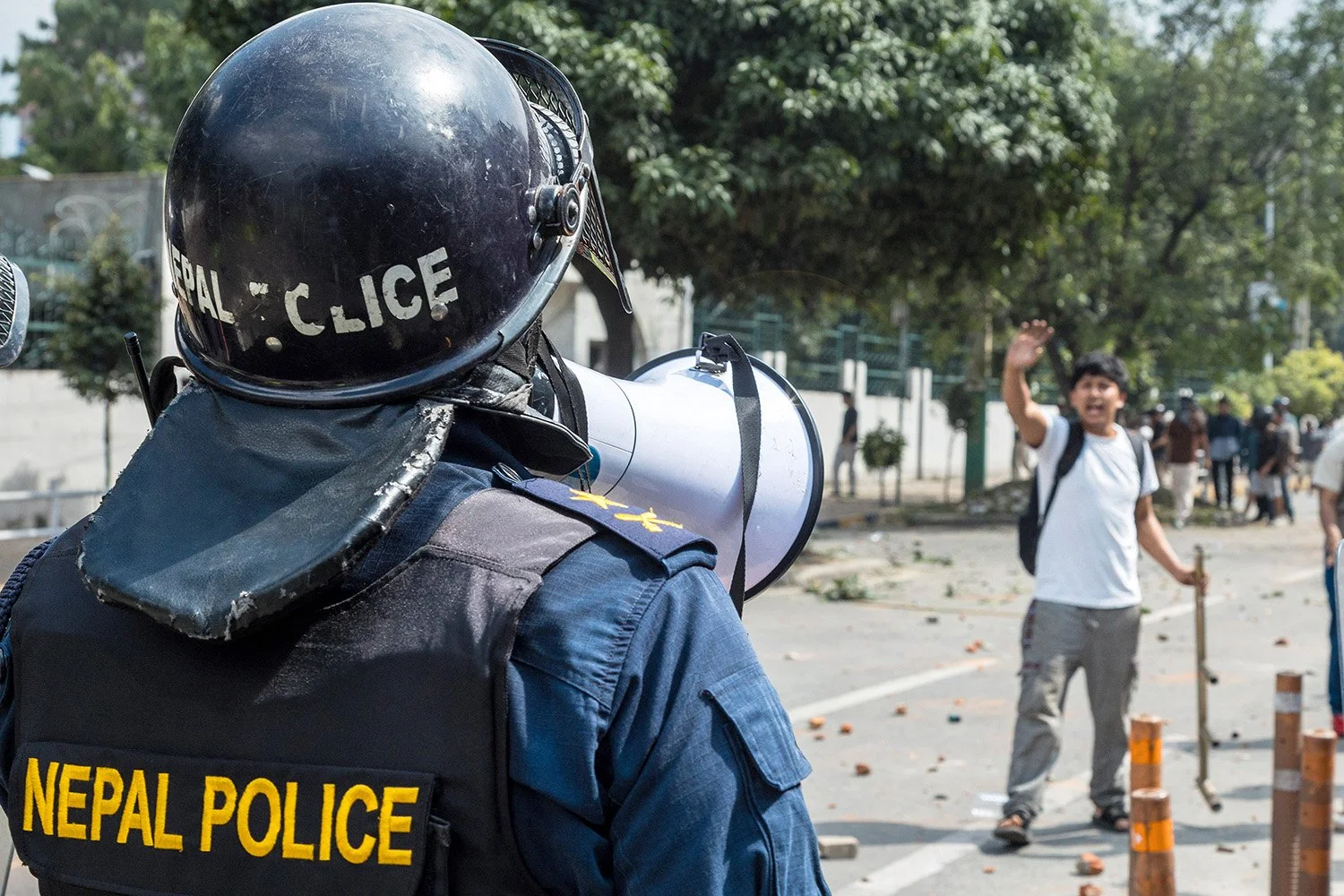 [Act I: Assembly]. A police officer commands a protester to yield through a loudspeaker.
